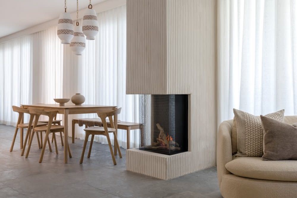 A mid-century modern dining room with a chic fireplace as the focal point. The room is furnished with iconic mid-century modern pieces in neutral tones, complemented by warm, ambient lighting.