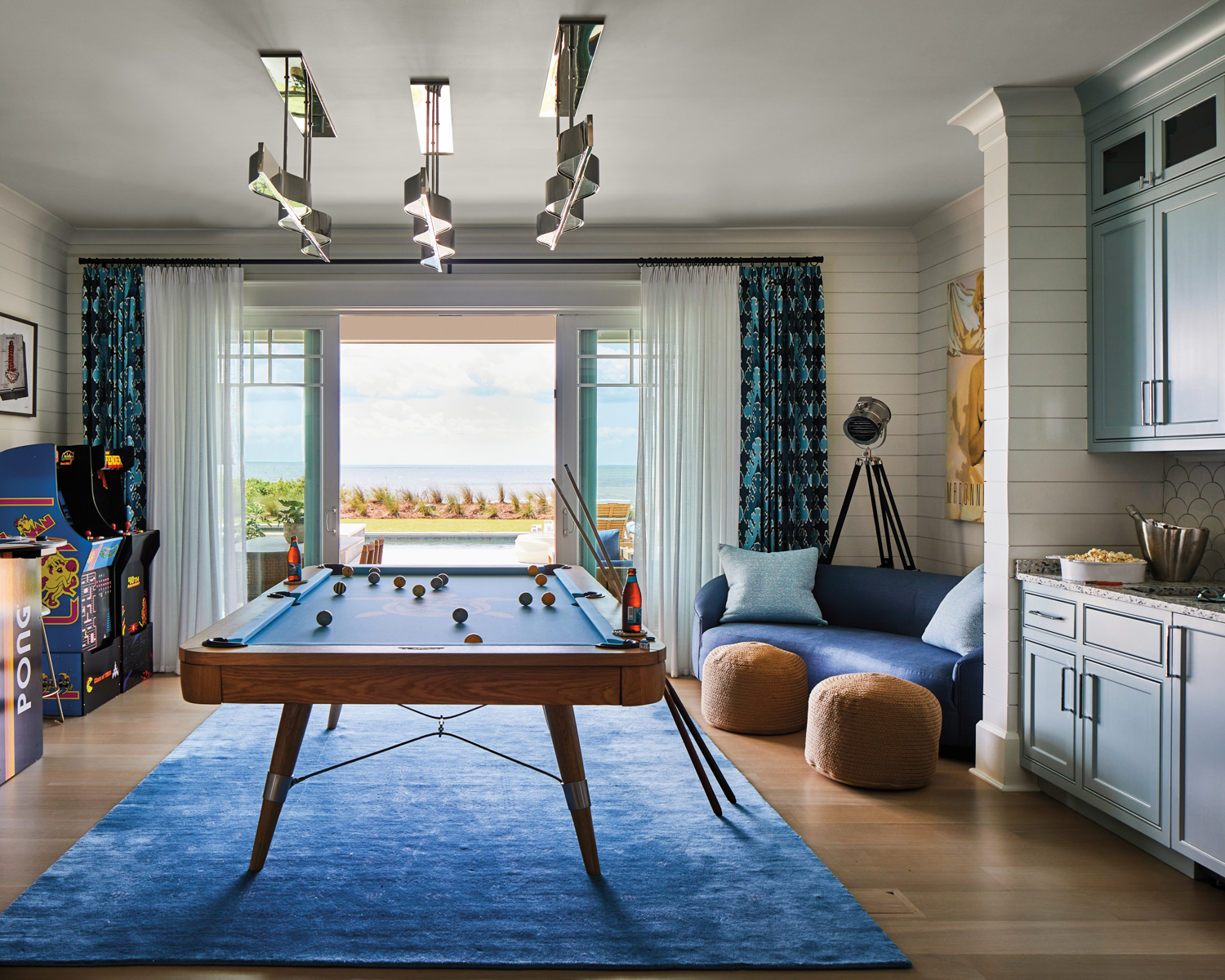 A gaming room filled with a pool table, pinball machines and other games beside sliding patio doors