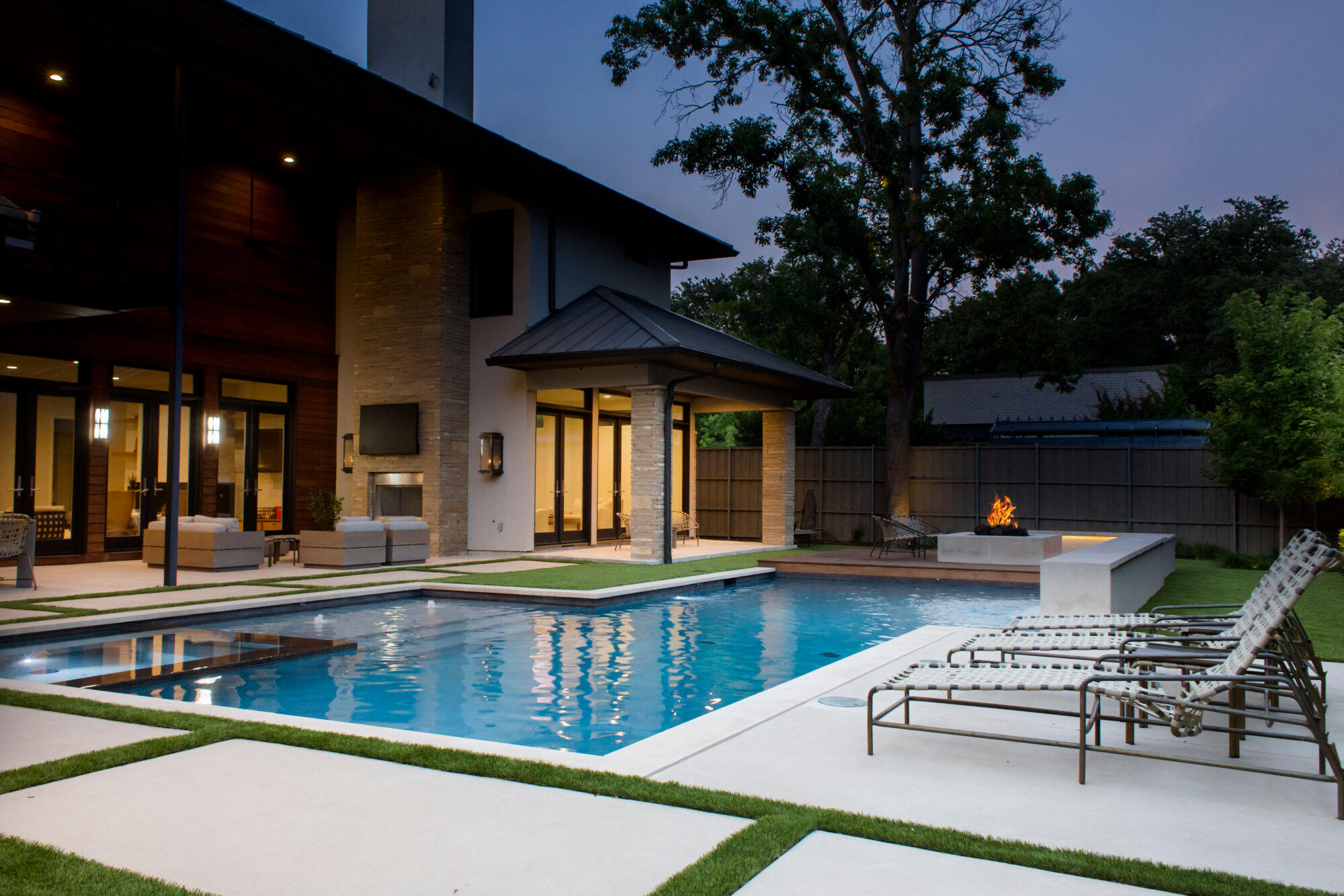 Nighttime poolscape with warm lighting and patio furniture