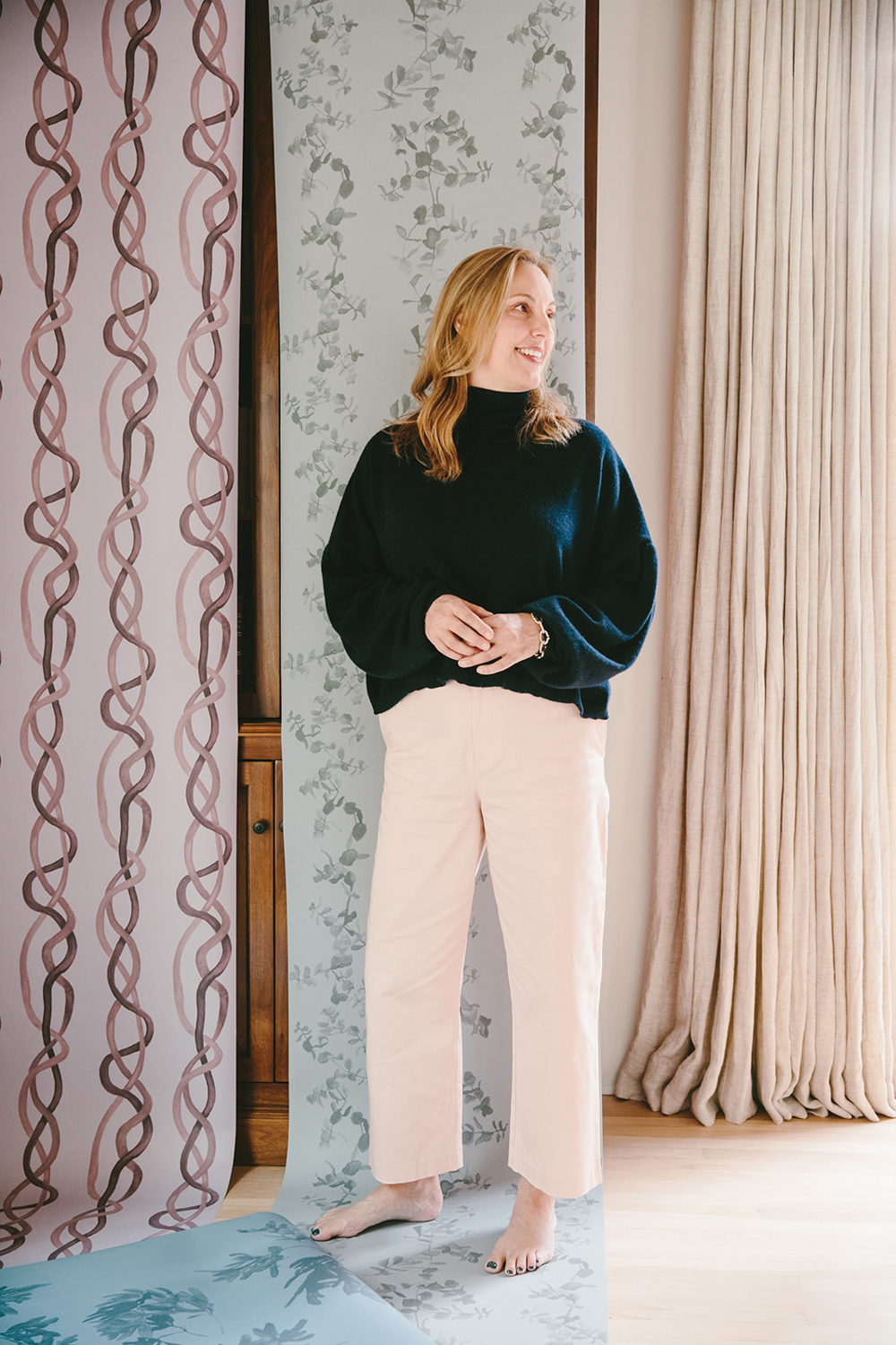 Jennifer Miller standing in front of tall swaths of her patterned wallpaper designs