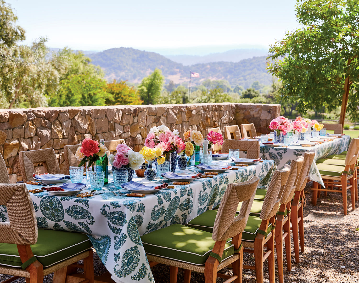 Outdoor summer table setup with floral centerpieces, green cushions and a leaf-print tablecloth