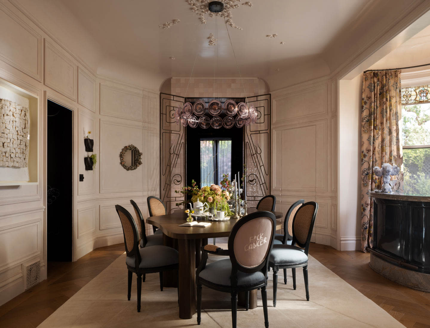 Elegant dining room with a round table set for tea, surrounded by six chairs. A floral centerpiece adorns the table under a modern chandelier.