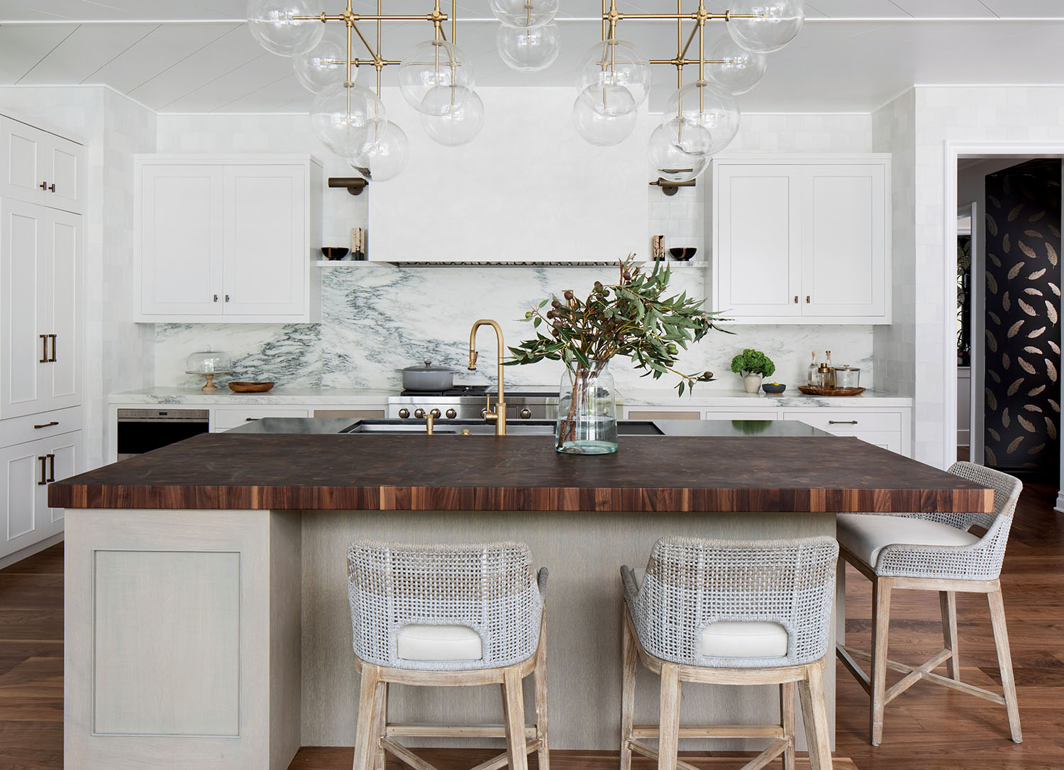 A kitchen with white cabinets, an island with wood countertop and high-top stools.
