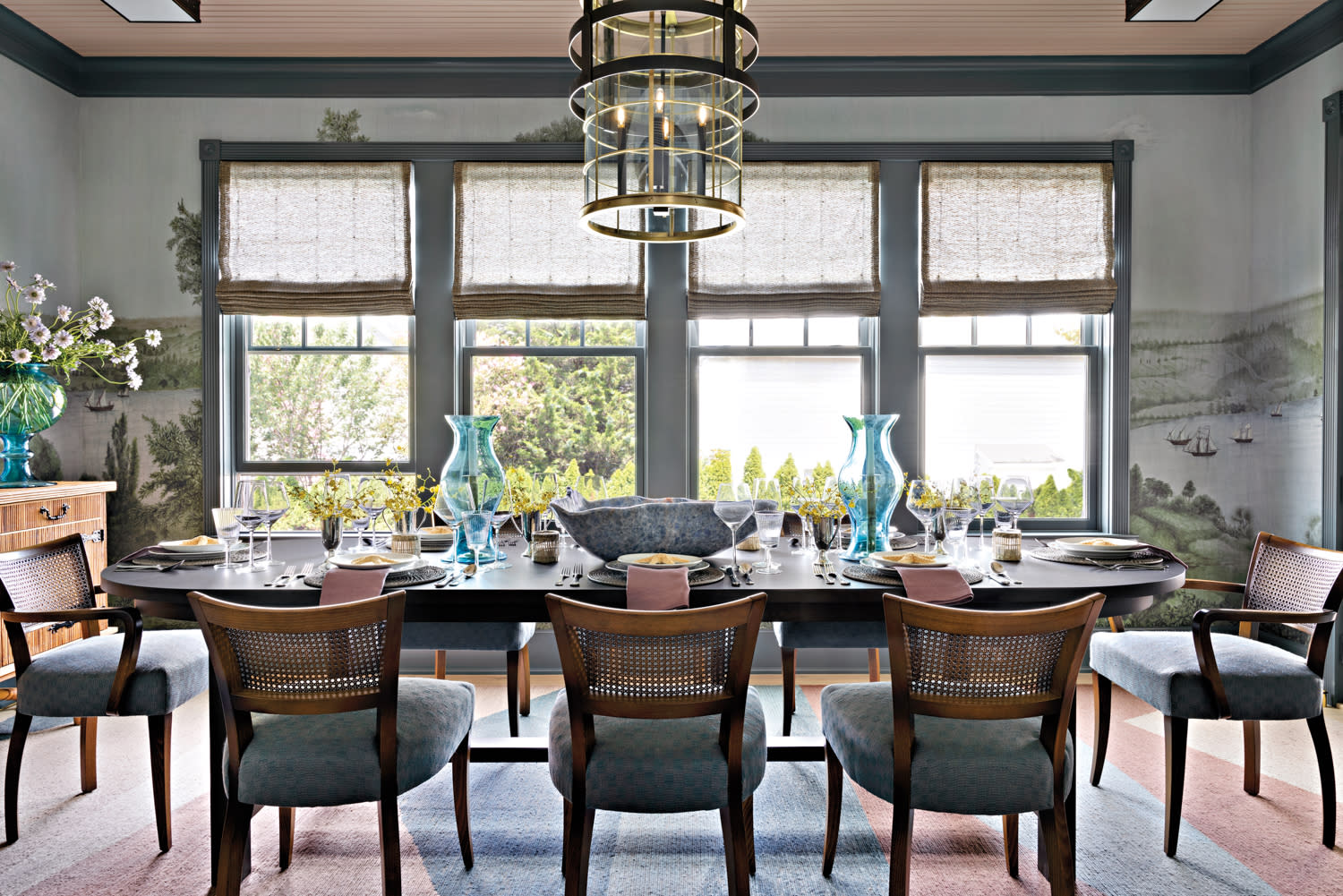 scenic wallpaper lines a dining room with cane-backed dining chairs