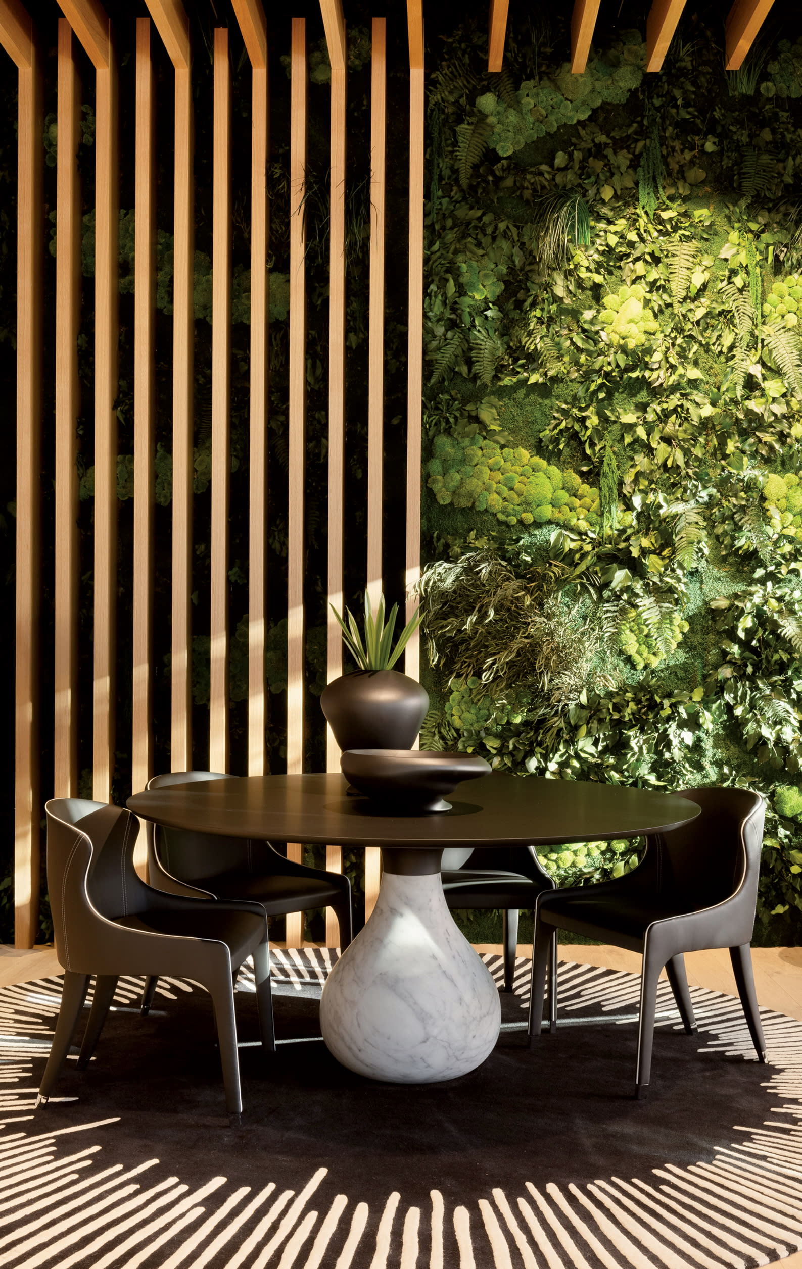 round dark wood dining table surrounded by leather chairs in front of a paneled wall fixture