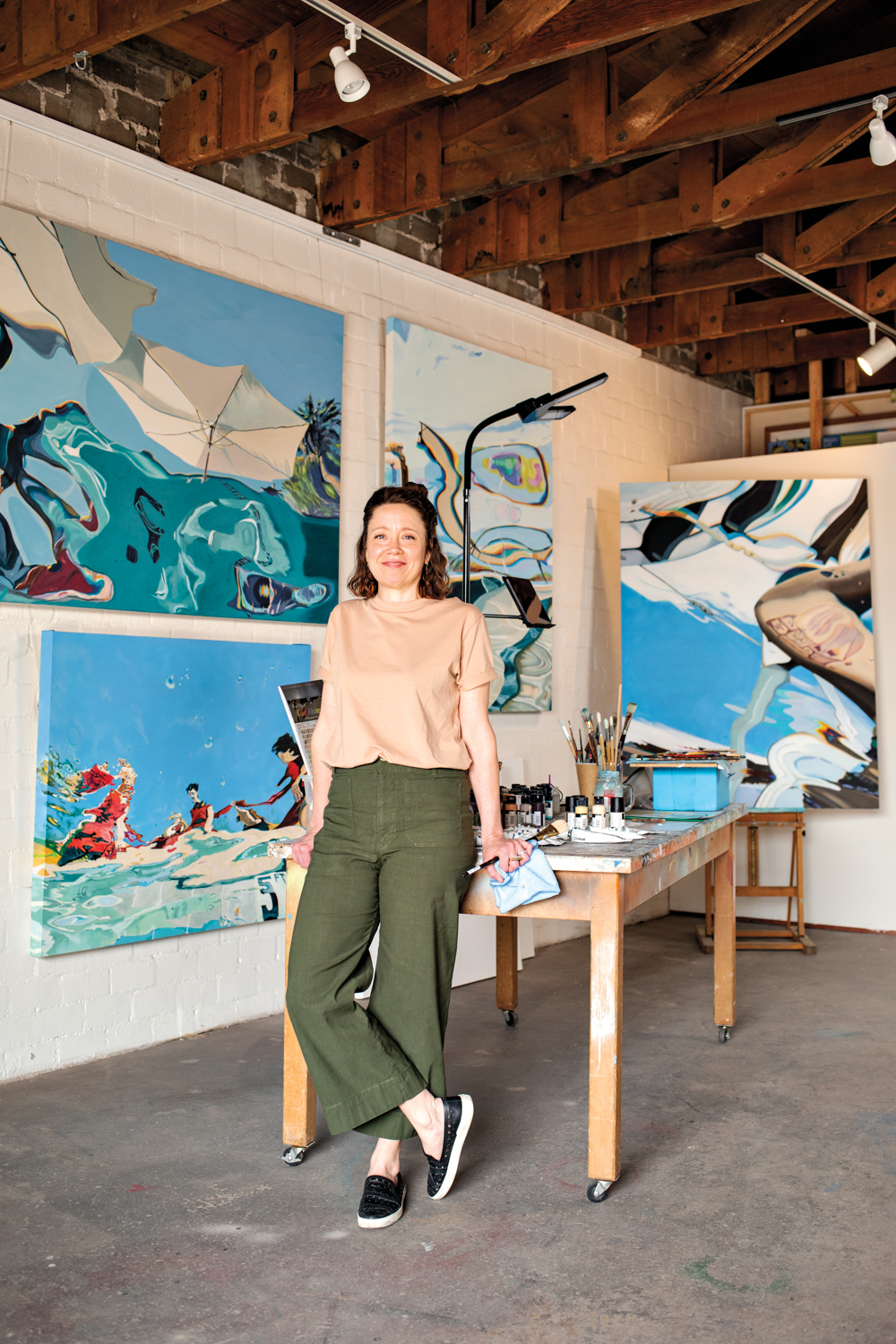 Artist Abbey Messmer standing in front of a grouping of paintings