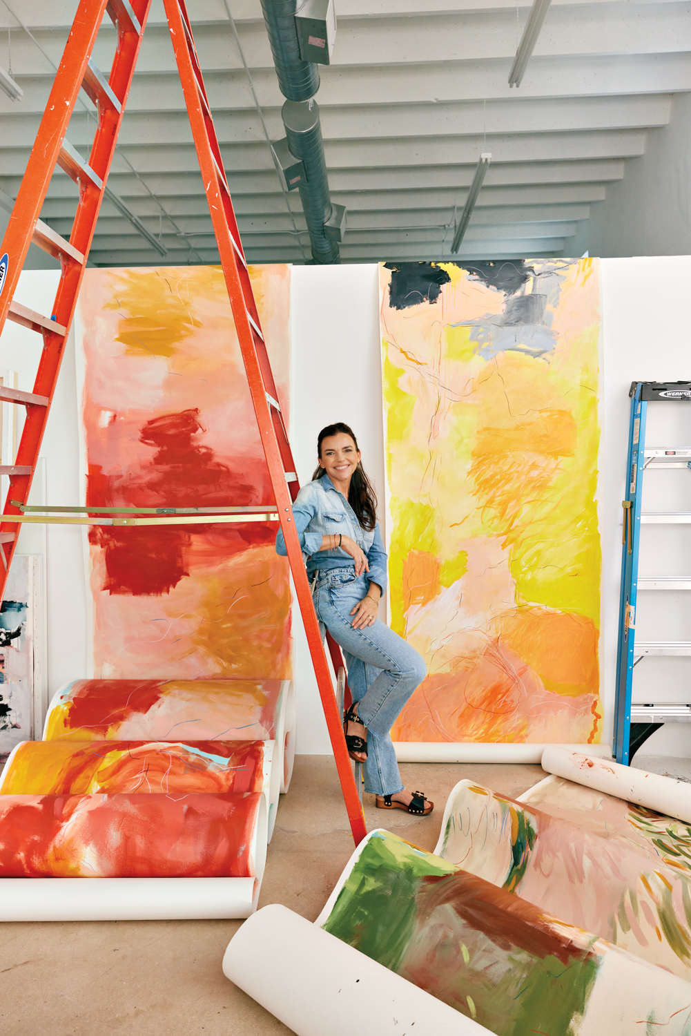 Verónica Pasman smiling on a ladder in her studio surrounded by her colorful 33-foot-long paintings