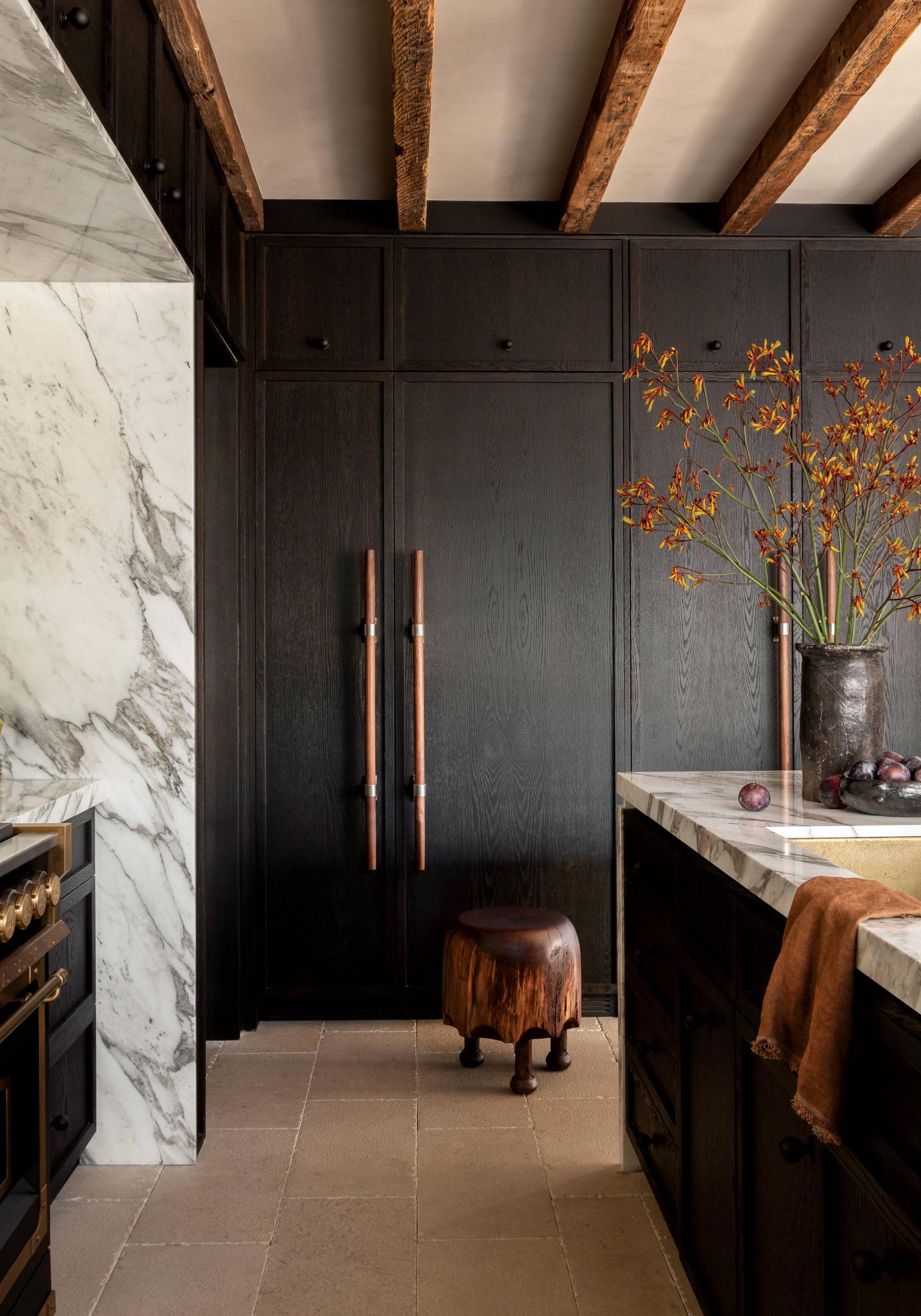 kitchen with black cabinetry, white and grey marble island and exposed wood beams