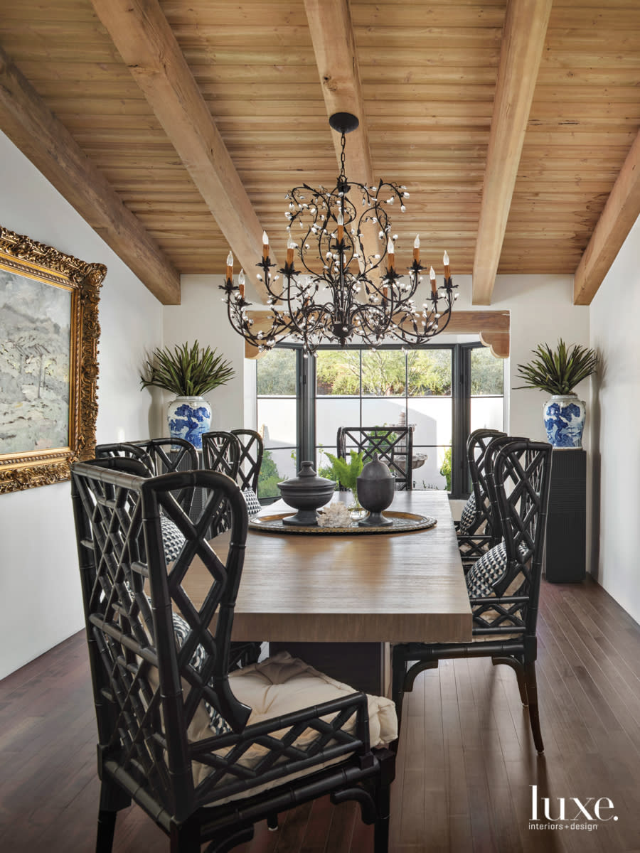 A symmetrical dining room is decorated with intricately designed black chairs and a chandelier.