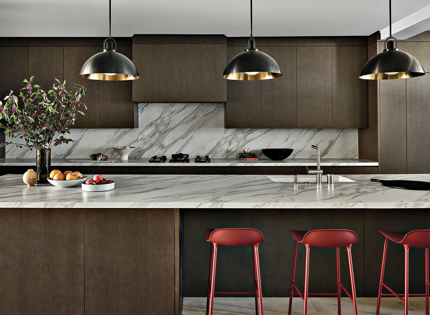 modern kitchen with porcelain counters and a trio of pendants above an island with red barstools