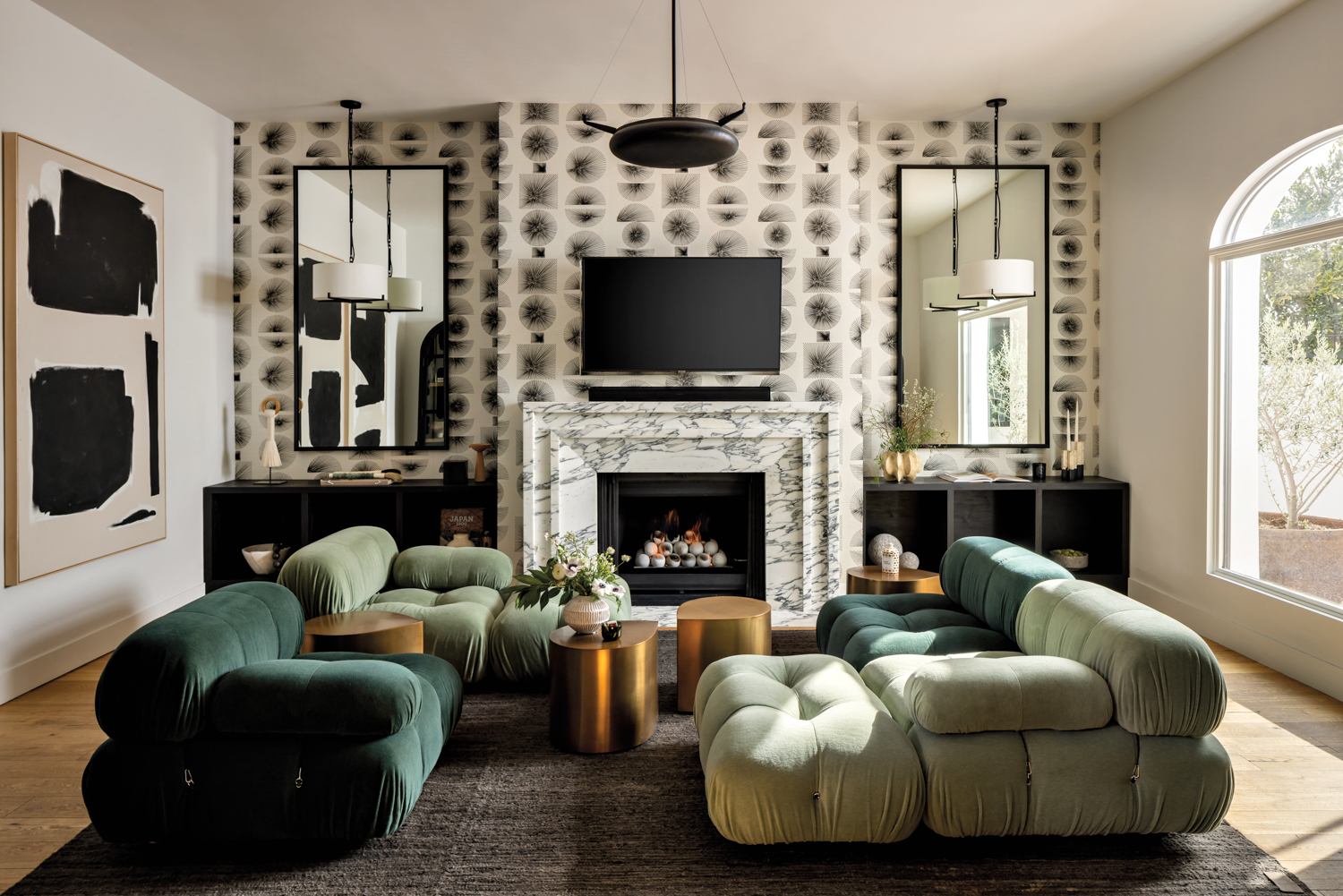 Living room with geometric wallcovering, green velvet sofas, white fireplace and black built-in cabinetry