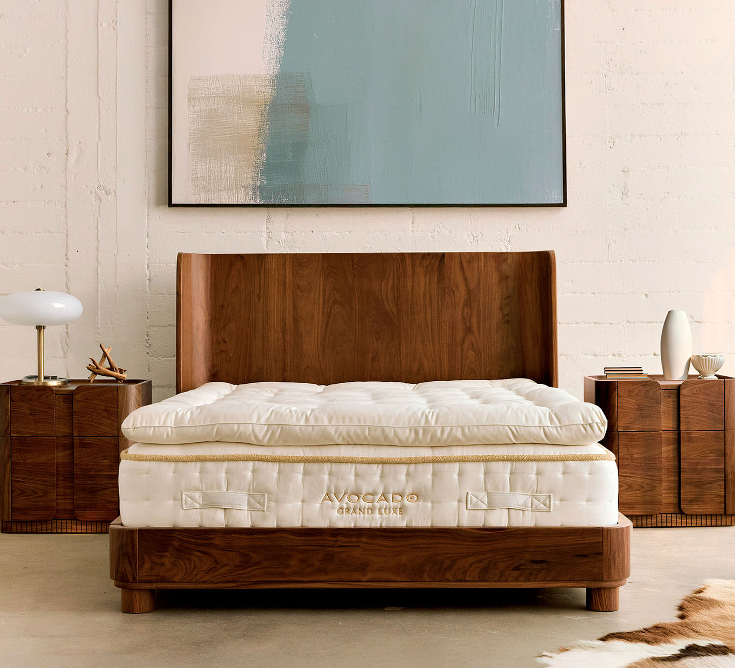 A mattress sits on a wooden bedframe flanked by two matching nightstands, with framed art overhead.