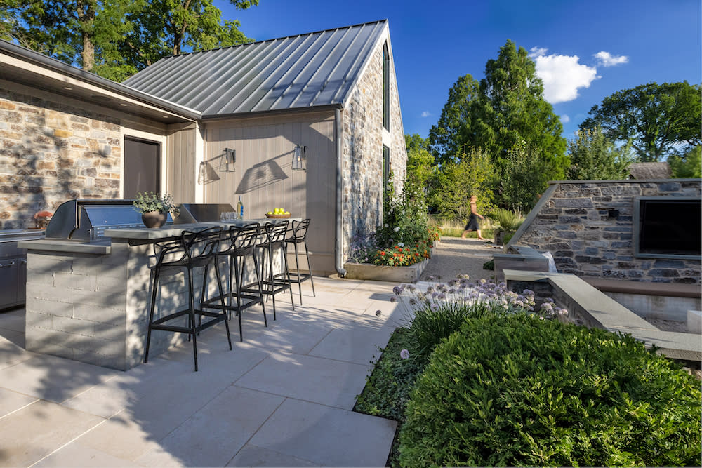 Rustic outdoor kitchen with bar seating and lush landscape.