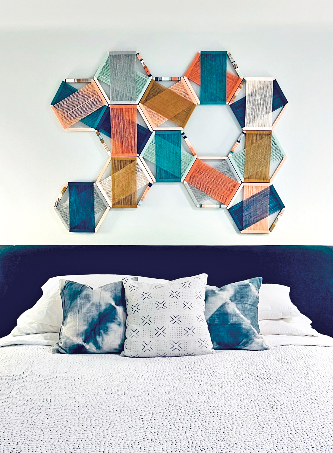 installation of colorful fiber artwork in hexagonal frames above a bed