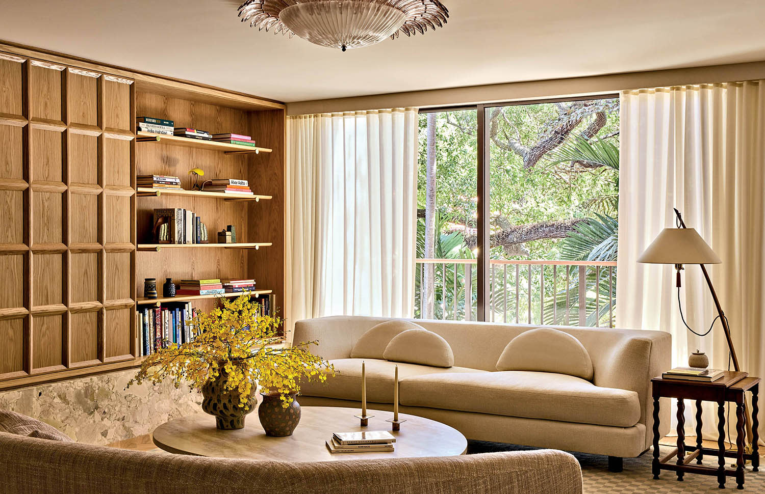 Couches sit on either side of a round coffee table near a window and wood built-in bookshelves.