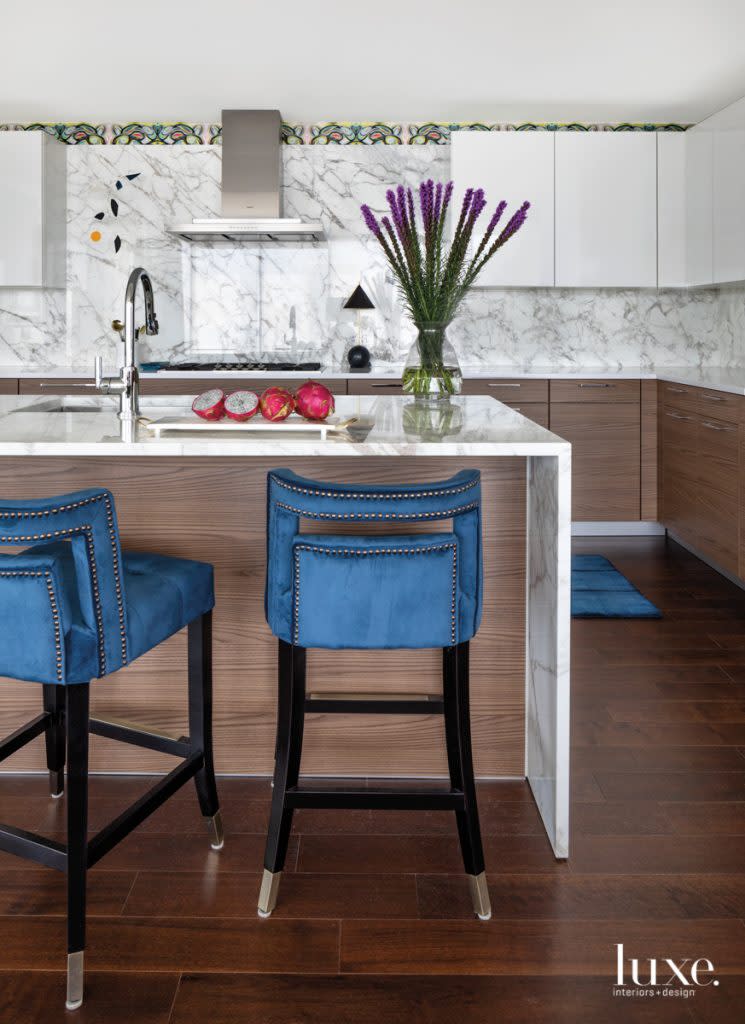 In the kitchen, which was designed by Rottet Studio when the high-rise was built, punches of color punctuate the crisp, contemporary finishes. Polished Calacatta marble covers the island and backsplash, melding with upper and lower cabinetry by Poggenpohl. Near the vent hood by Gaggenau is a Mark Leary mobile.