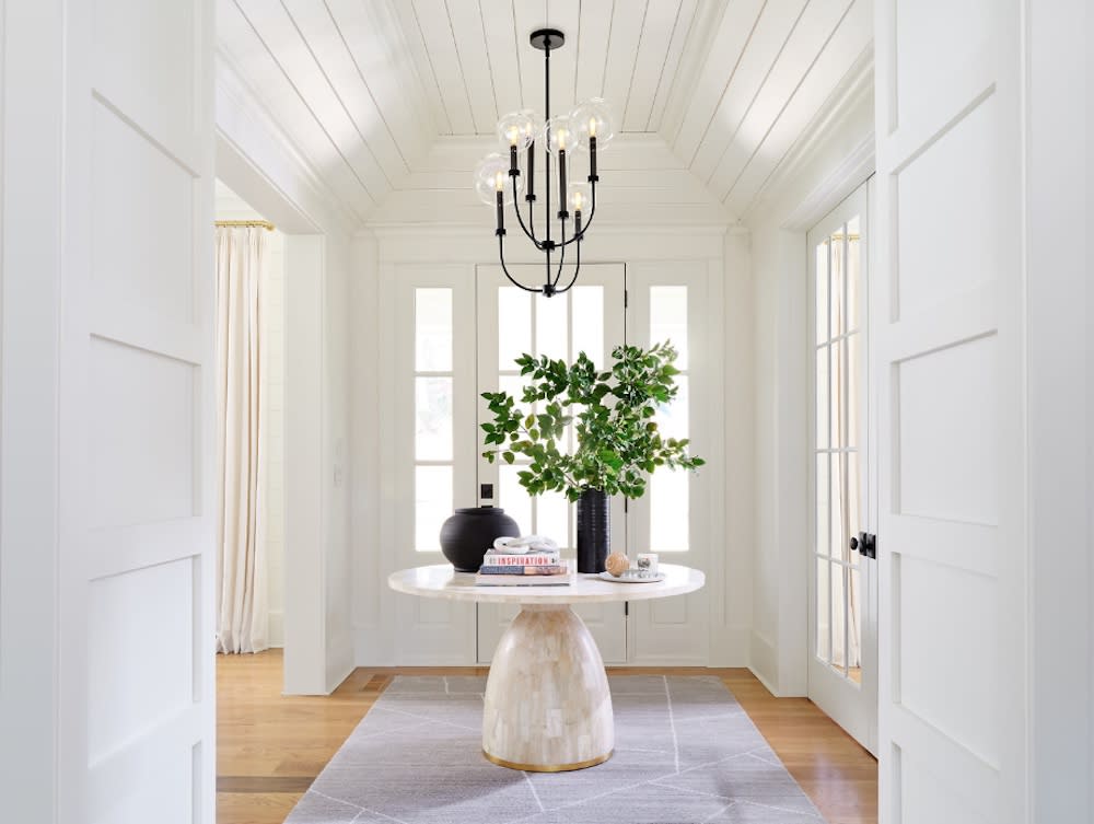 A white hallway with a chandelier and decorative circular table.