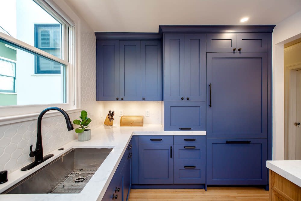 An image showcasing a kitchen with striking blue cabinets paired elegantly with pristine white countertops. The black faucet and fixtures provide a sleek accent against the vibrant blue and white color scheme, adding a touch of modern sophistication to the space.