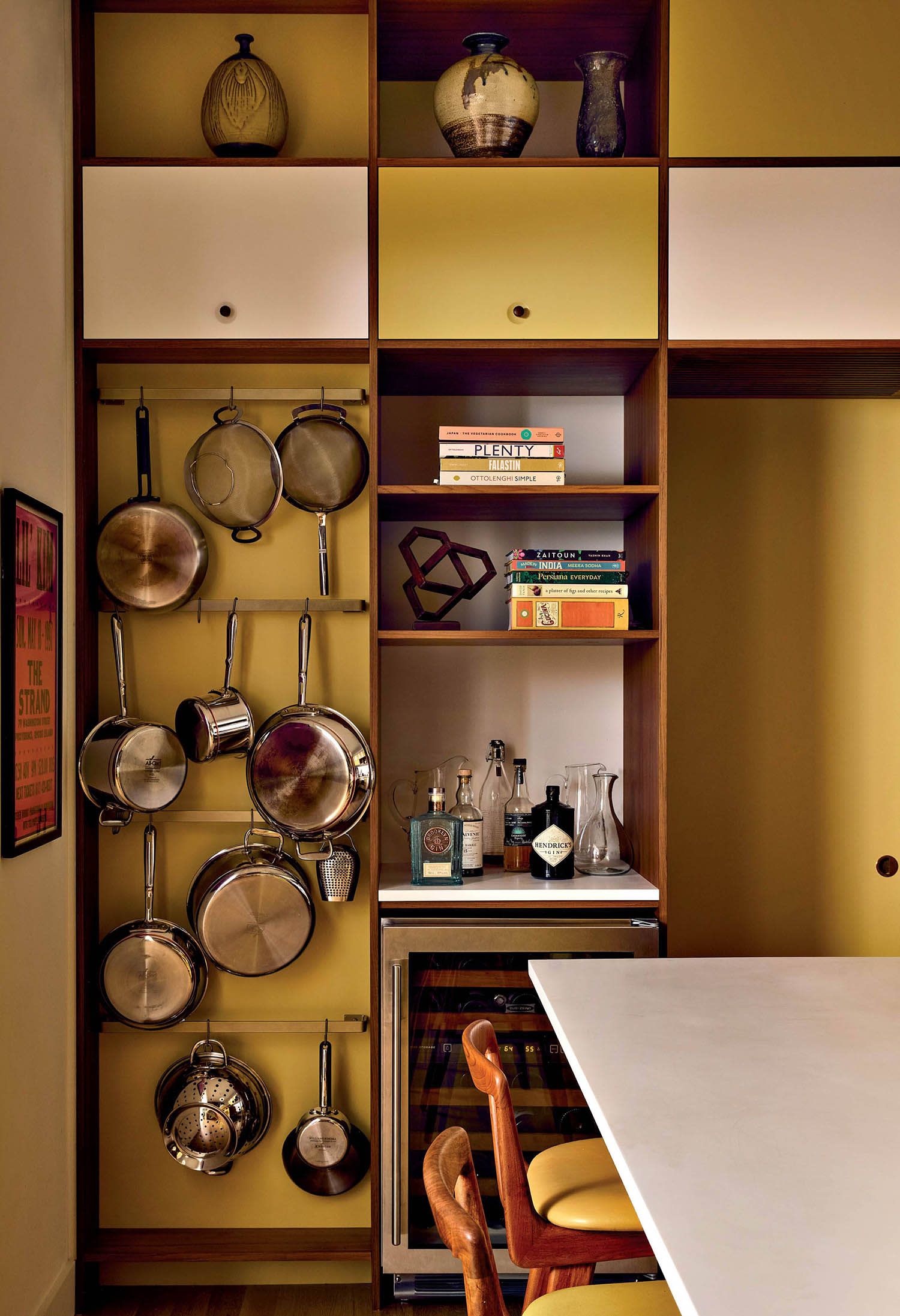 A kitchen nook with alternating yellow-and-white painted cabinets, shelves and hanging cookware. 