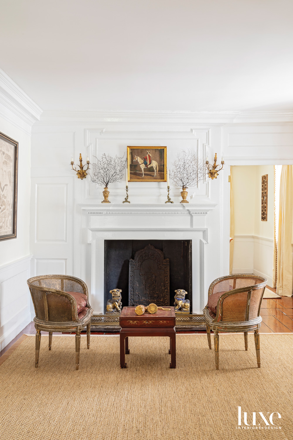 Fireplace with framed oil painting, pair of chairs and coffee table by alexandra howard design