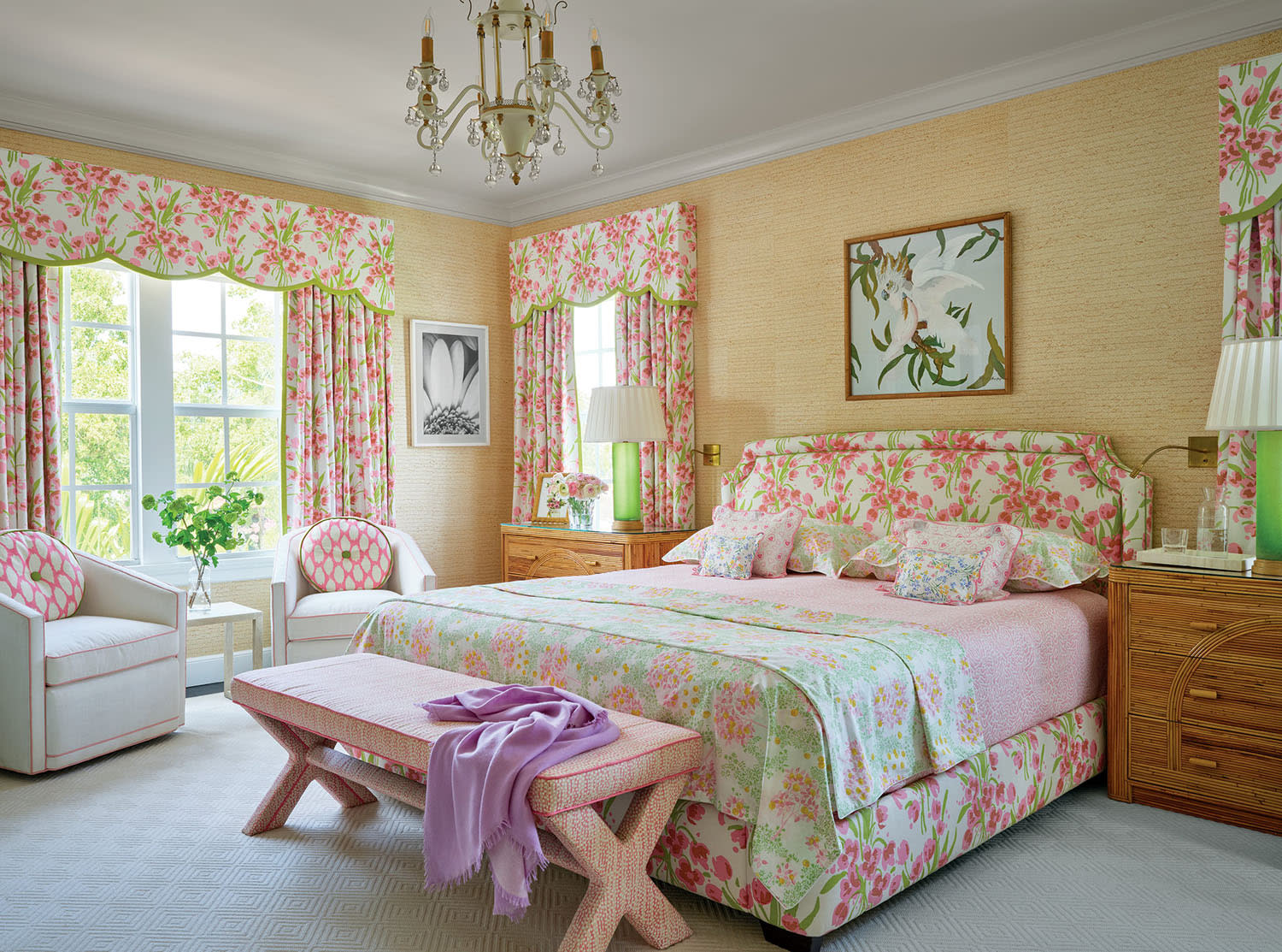 Floral-themed bedroom with pink and green accents. Features a large bed, patterned curtains, wooden furniture, a chandelier, and artwork on the walls.