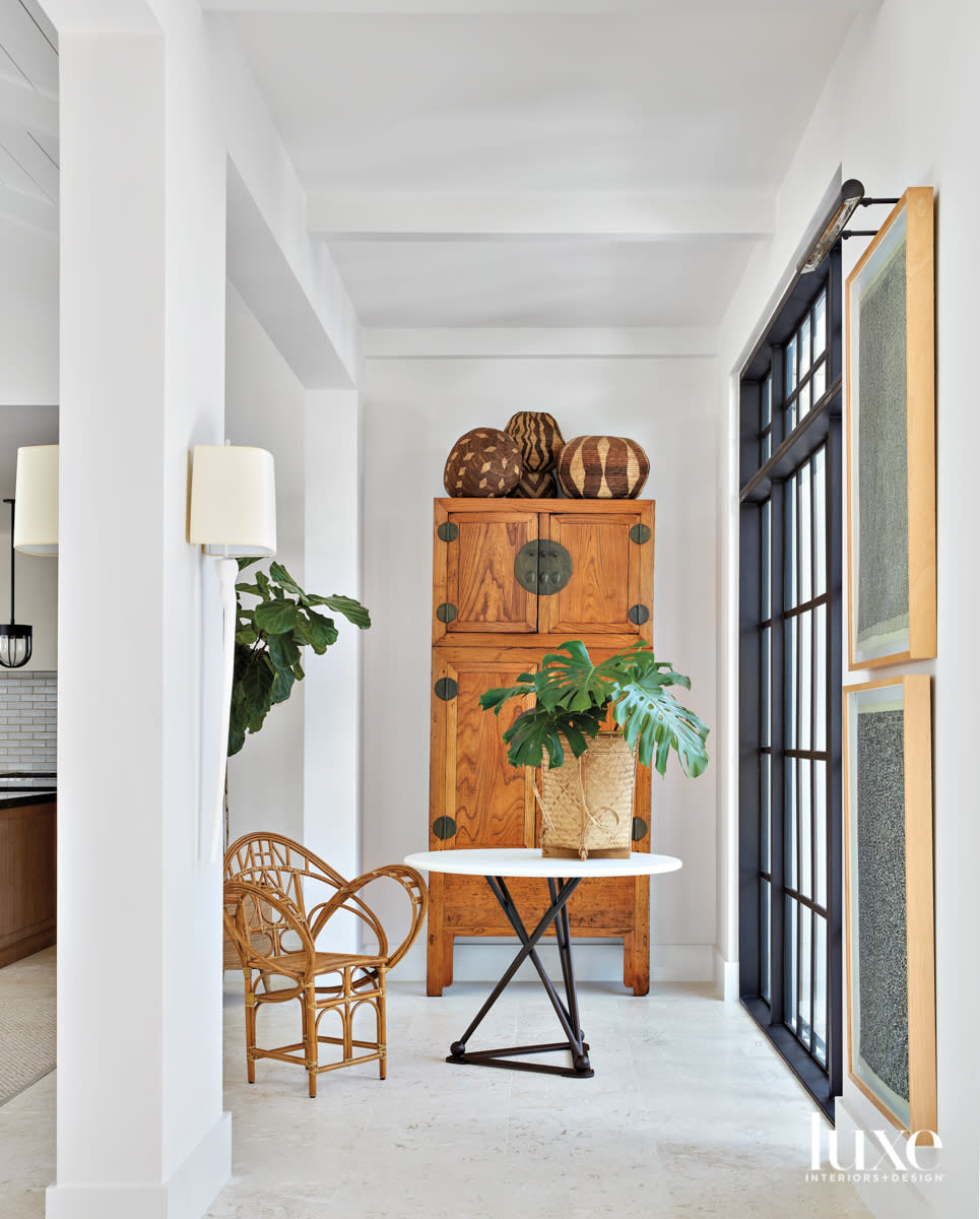 entryway with white walls, table, rattan chair and chinese armoire