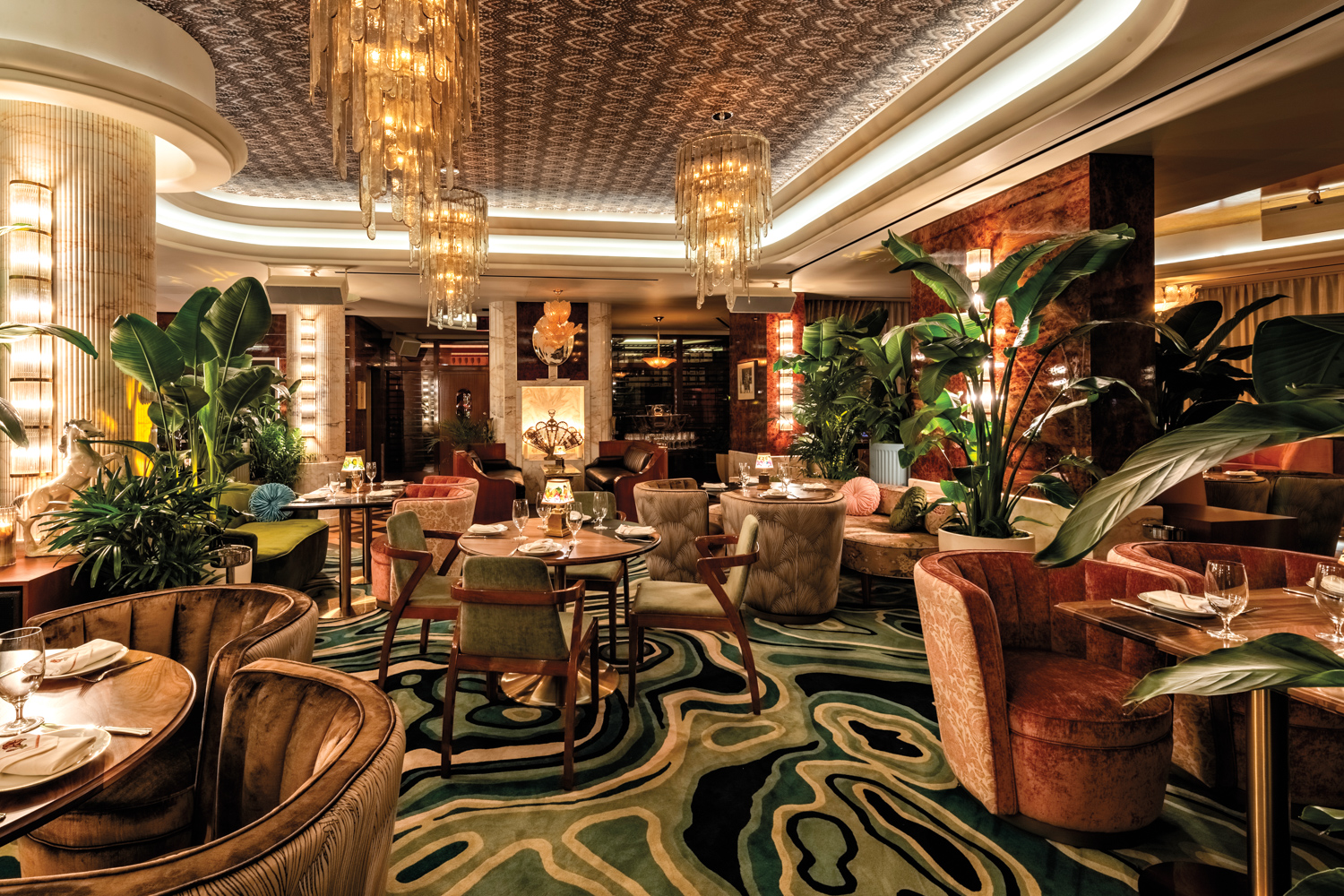 Dining area with green-patterned rug, Art Deco chandeliers, curved seating and dim lighting