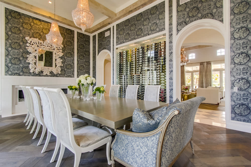 A spacious dining room with a large table, chairs, gold lighting and dark wallpaper.