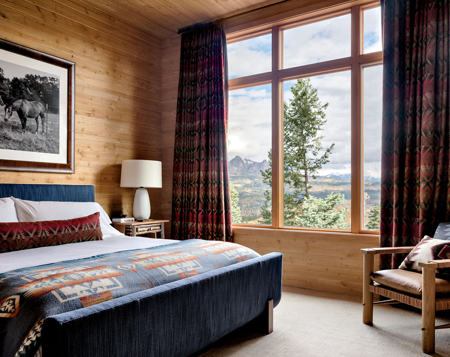 A bed with a printed blanket and matching pillow in a room with a window overlooking the mountains.