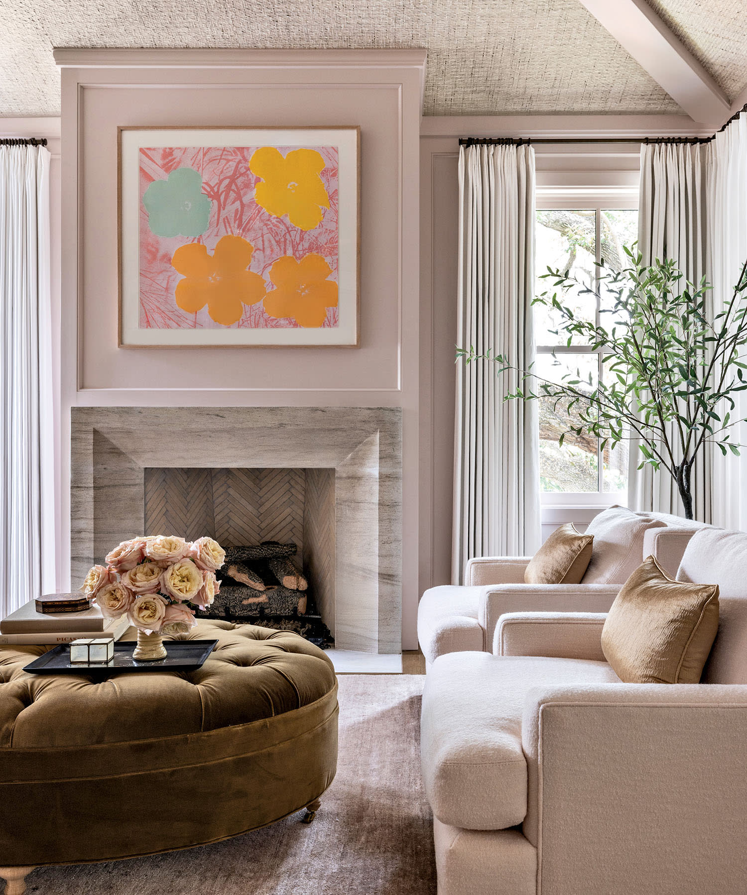 Elegant home office with a cozy fireplace, abstract floral art, beige sofa with brown cushions, round ottoman with flowers, and soft natural light.