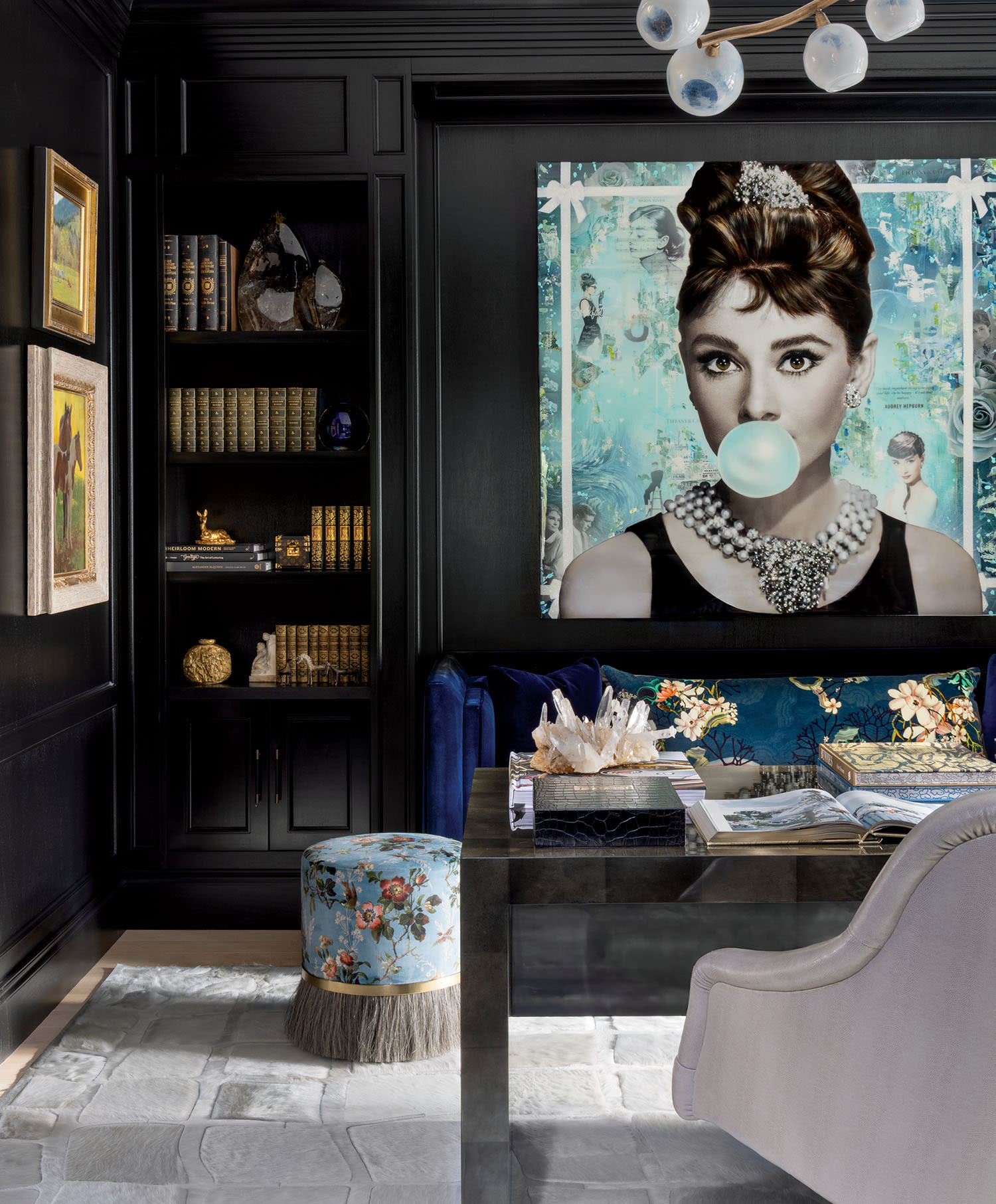 Elegant study with dark walls, a large portrait of a woman blowing bubblegum, bookshelves, a floral stool, and a plush chair, creating a chic atmosphere.