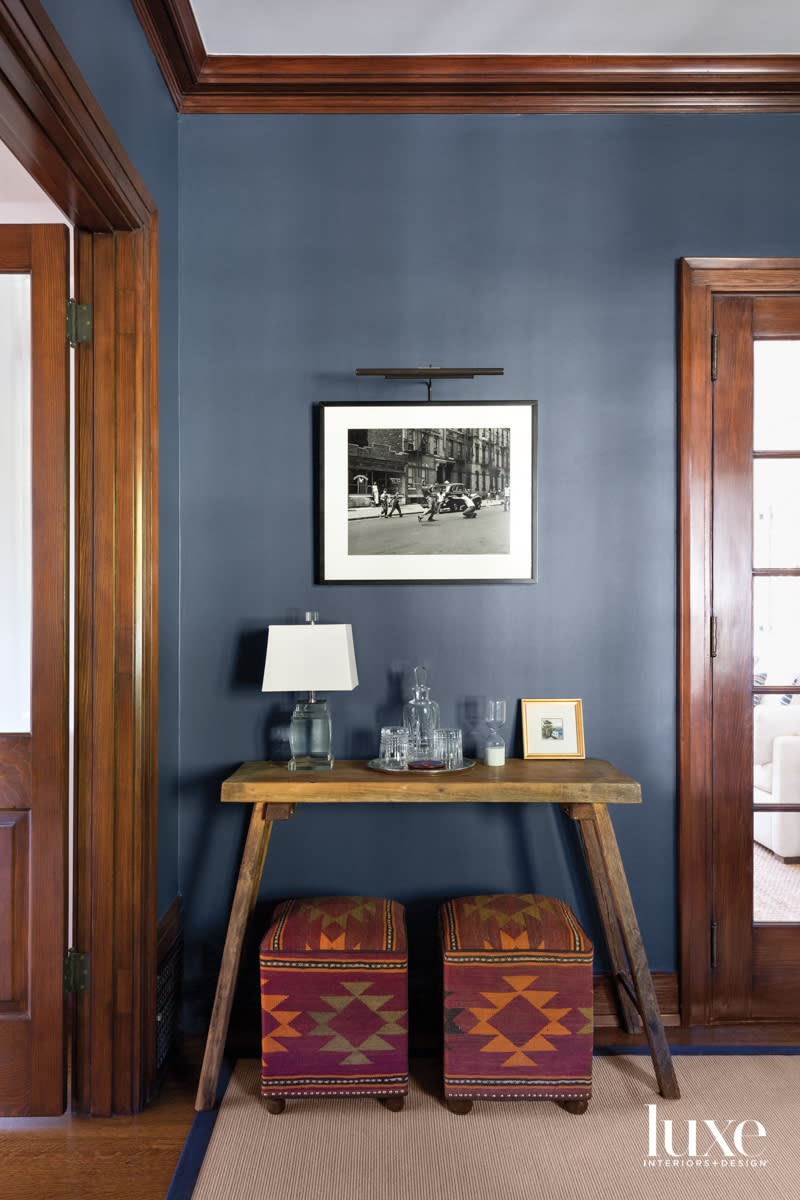 Detail of office painted blue with small console and upholstered ottomans