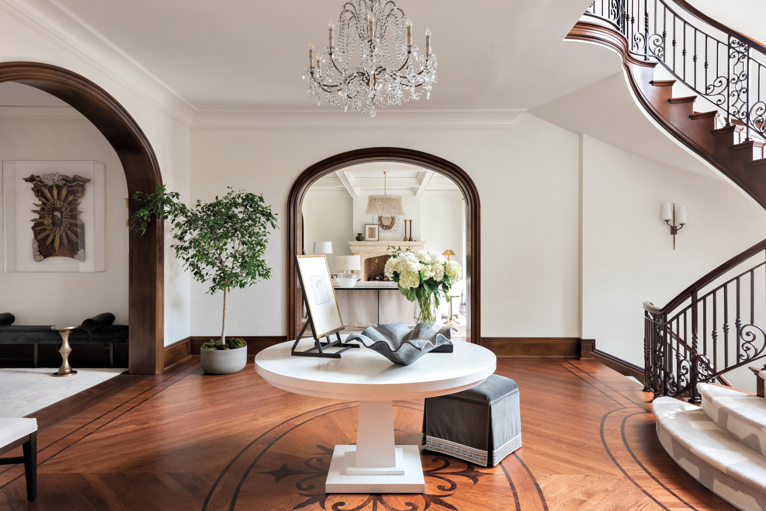 Central stair hall and foyer with wood floors, round center table, tree in corner and crystal chandelier