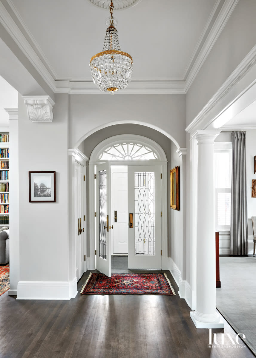 An entryway with a chandelier and a small red rug.