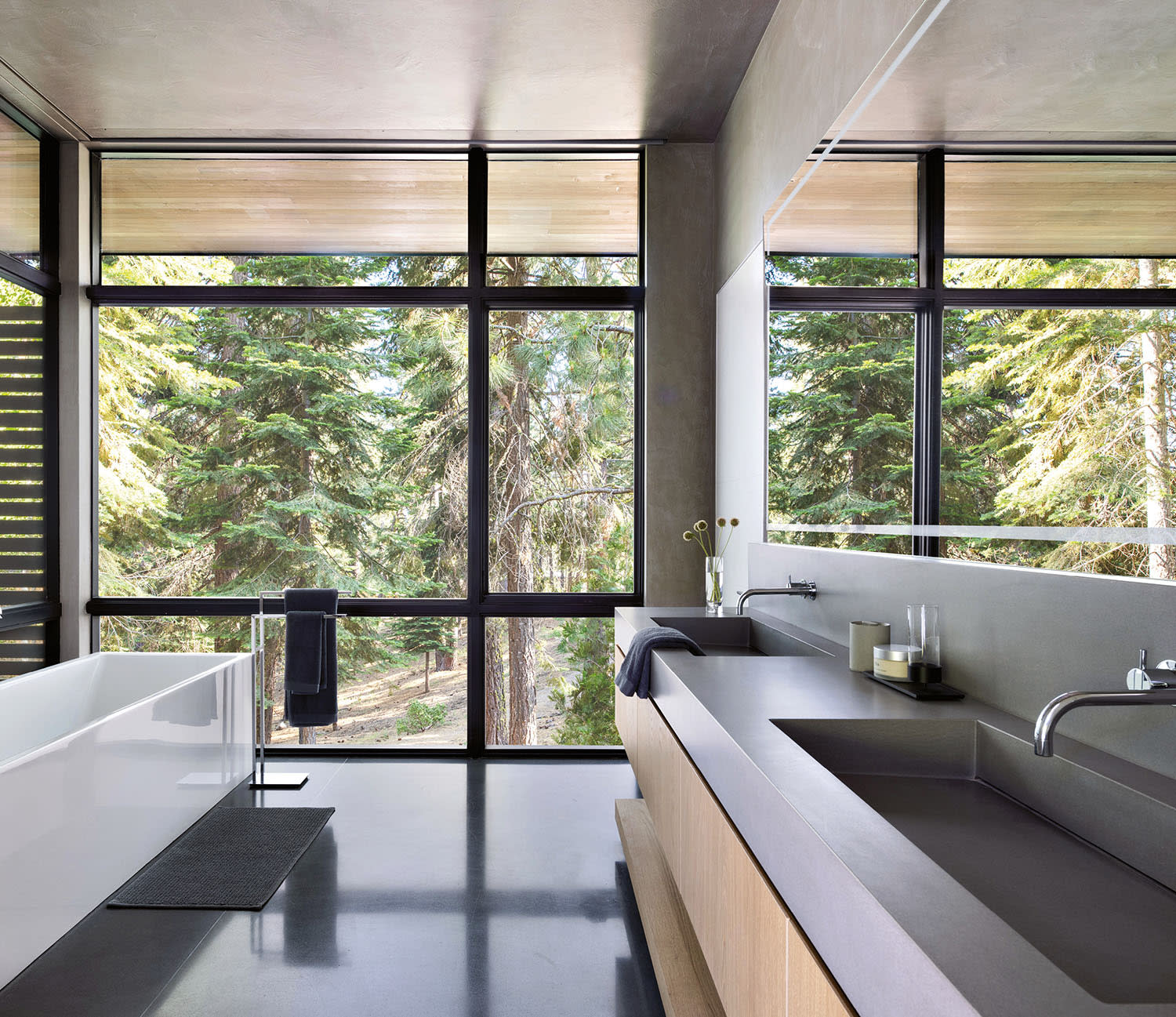 Modern bathroom with large glass windows showcasing a green forest