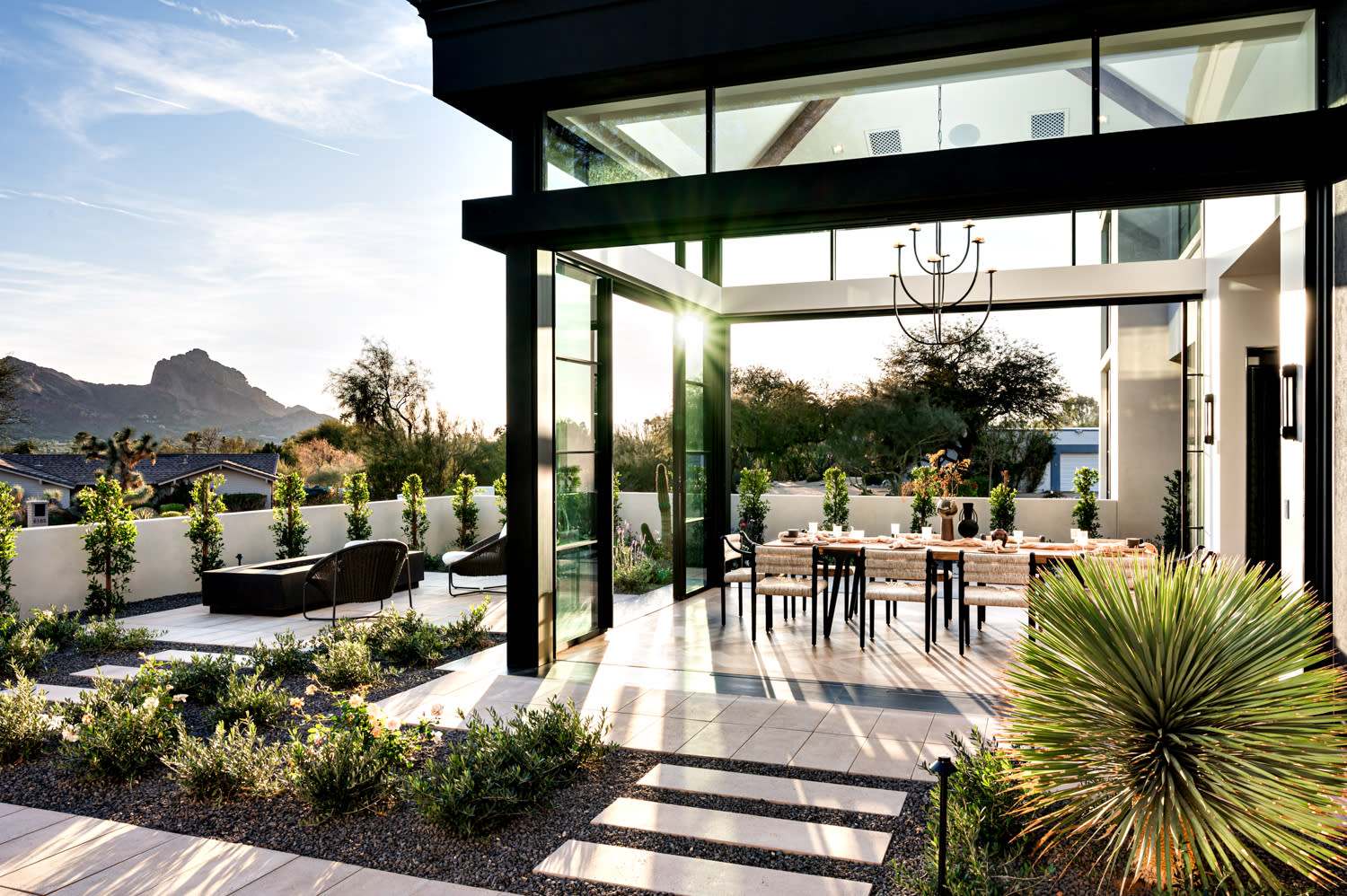 Modern patio with large glass doors leading to a dining area. Sunlight casts long shadows.