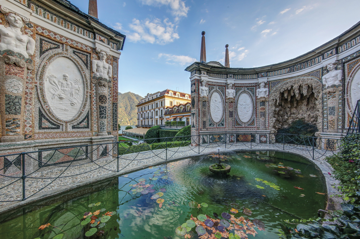 Pond with a fountain enclosed within a garden by decorative walls with statues and colored tiles