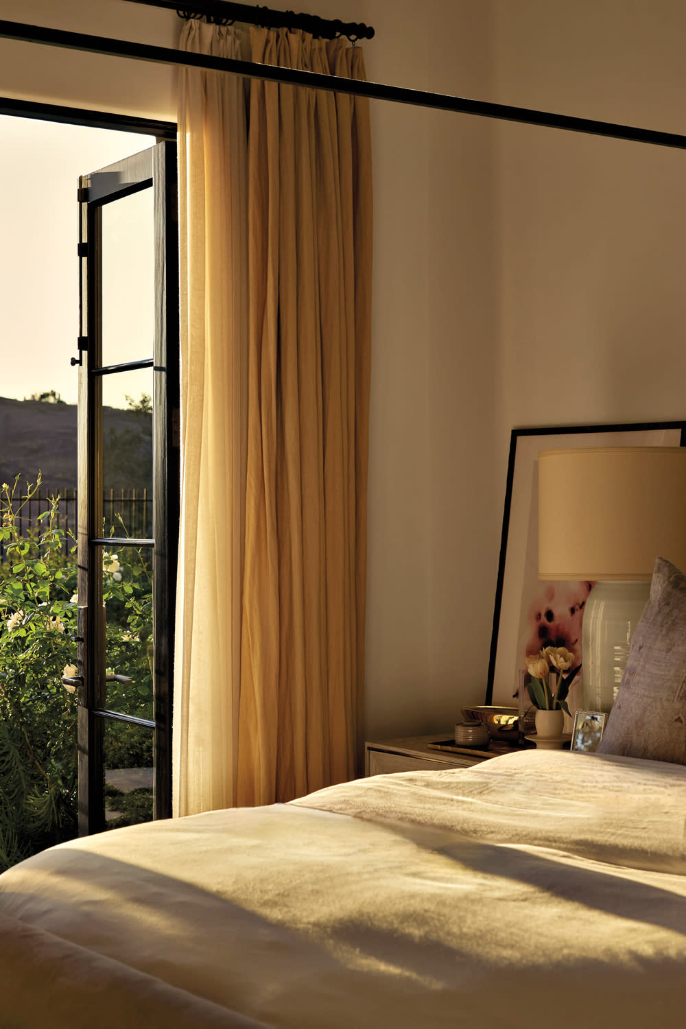 bedroom with doorway open to exterior seating area, sheer curtains and lamp in home by Nicole Green