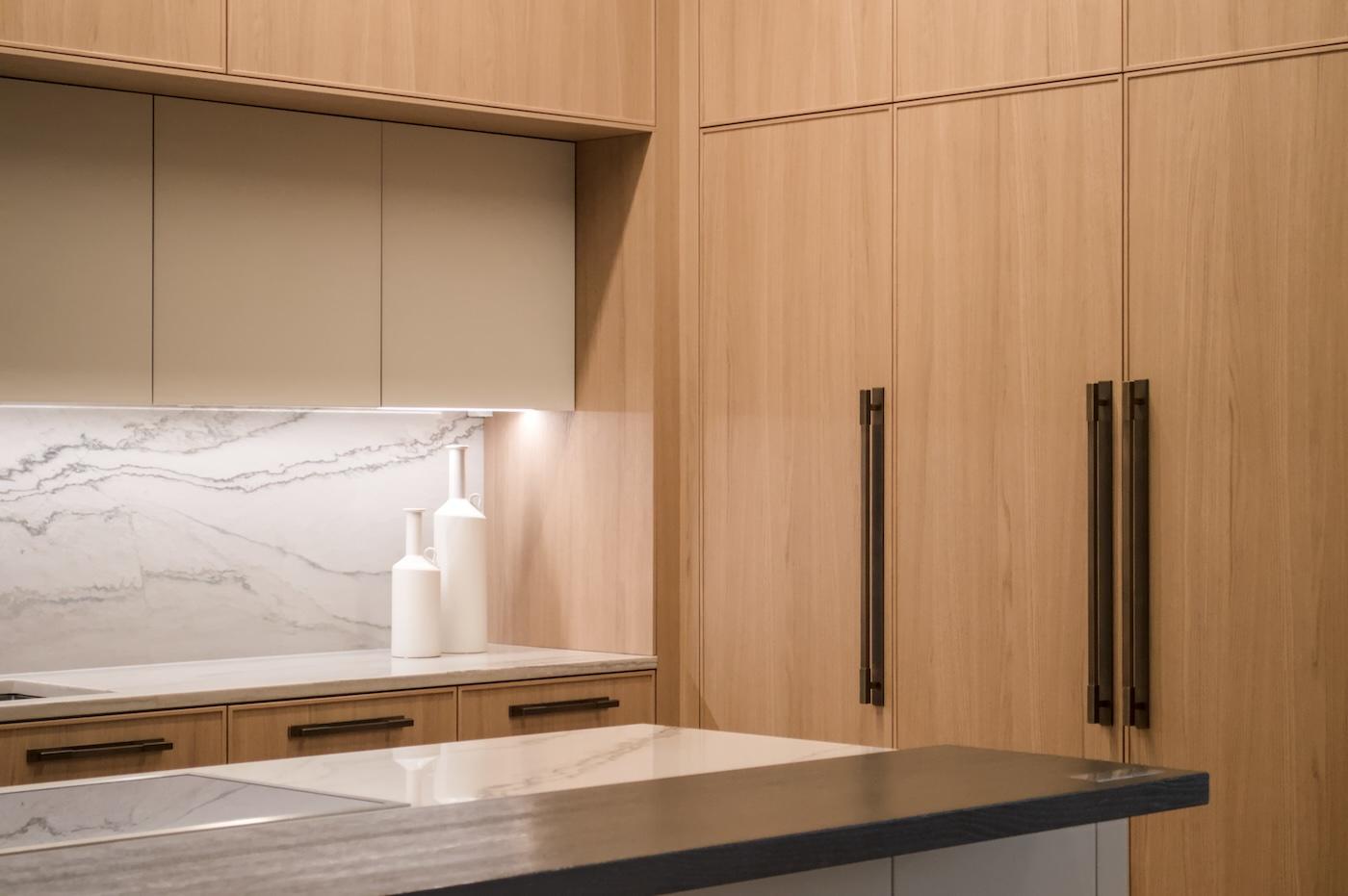 Minimalist kitchen with light wood cabinets, marble backsplash, white countertop, and two modern vases. The scene conveys elegance and simplicity.