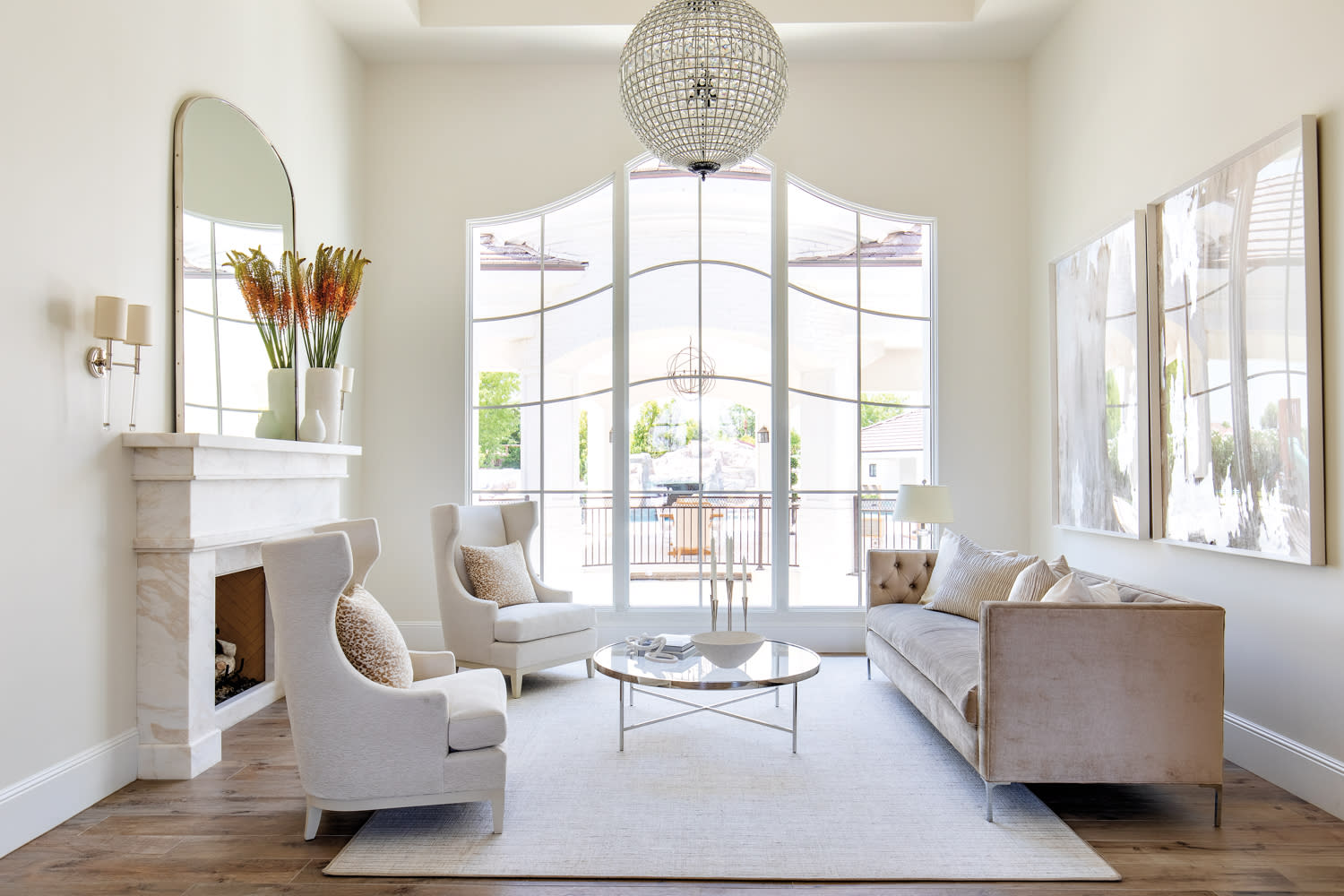 a living room with a velvet sofa, two armchairs, a round chandelier and a mirror above a stone fireplace