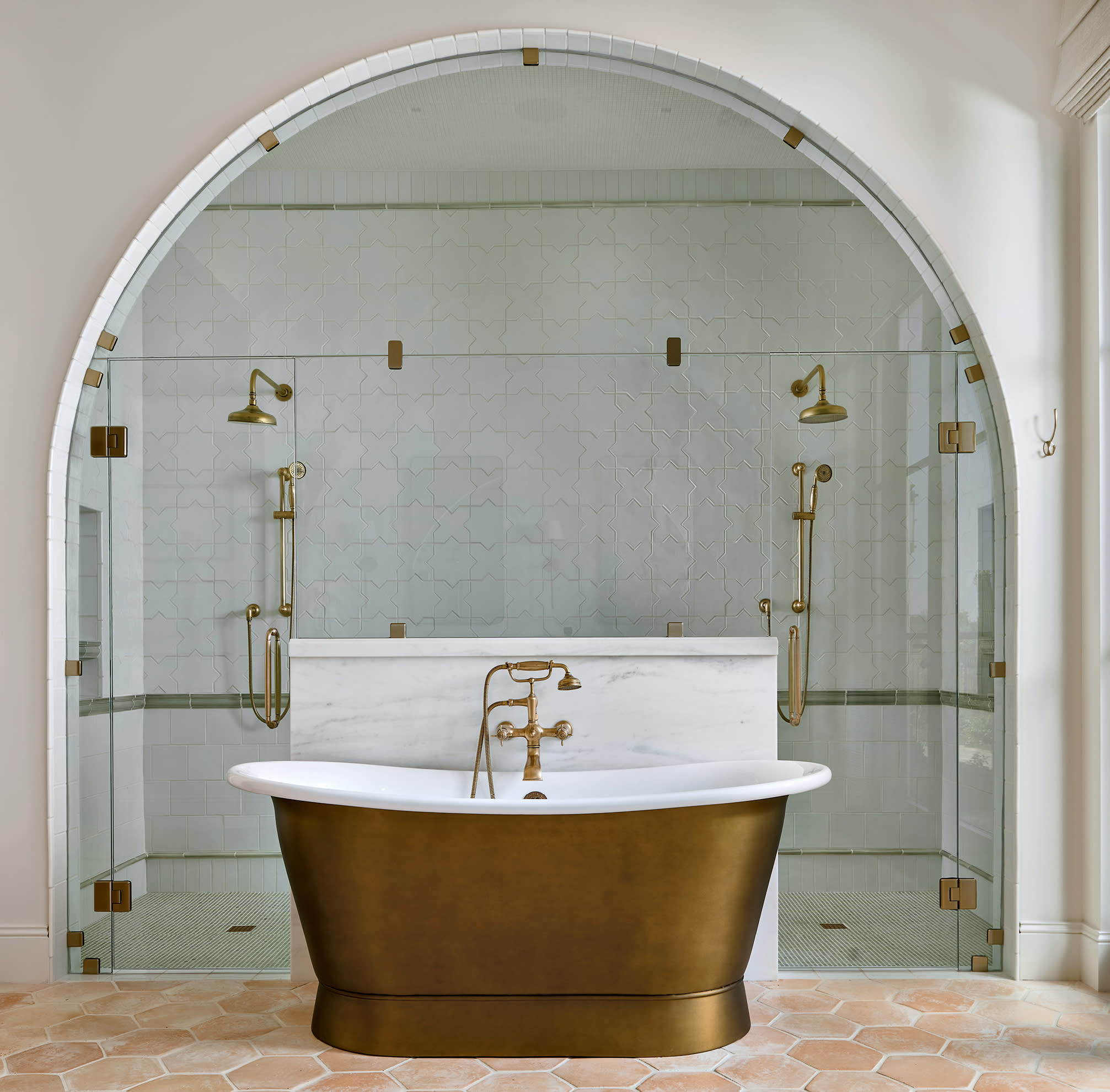 luxurious bathroom with an arched entrance to the shower behind a brass freestanding tub