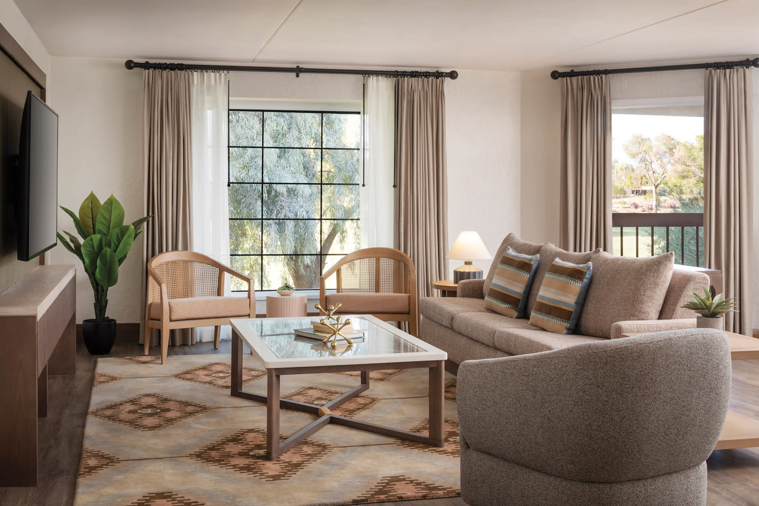 Hotel room sitting area with a gray sofa and wood armchairs atop a neutral patterned rug.