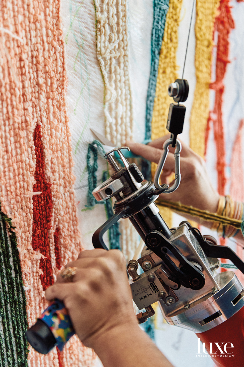 One hand maneuvering a tufting gun, another hand trimming excess yarn using scissors