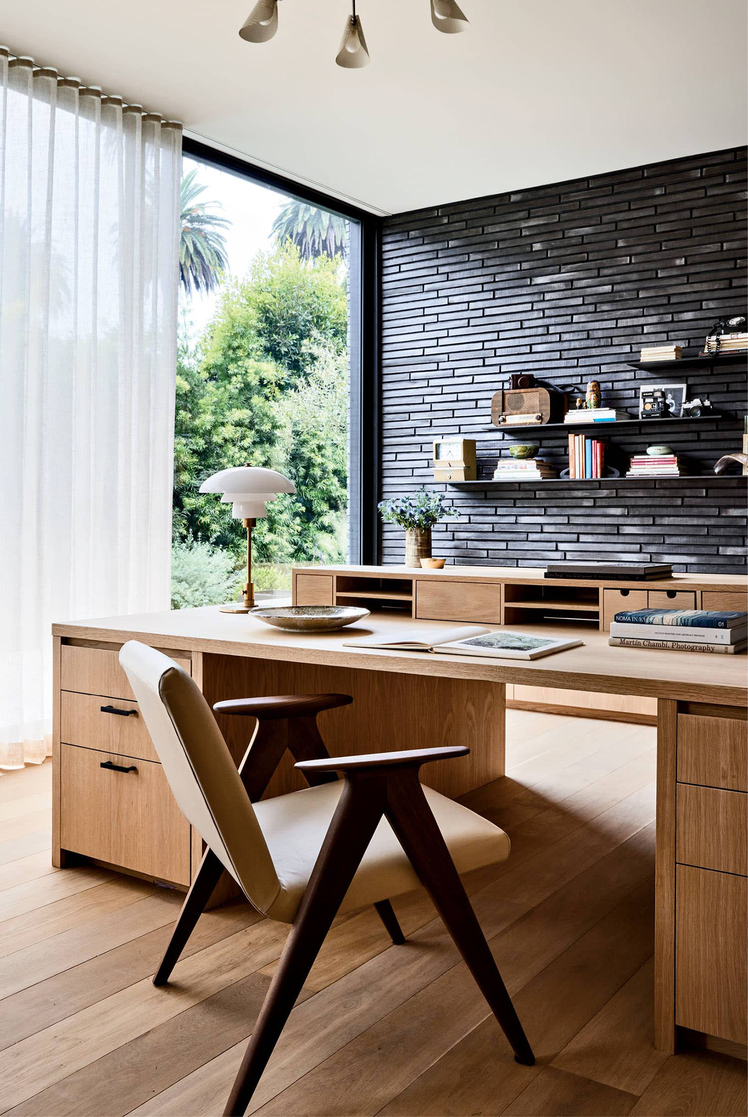 modern home office with an oak desk and a black-painted brick wall