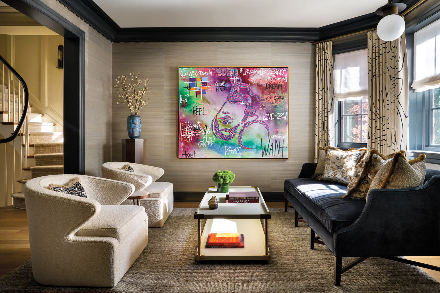 Living room with grass-cloth wallpaper, two ivory boucle chairs, navy velvet sofa and colorful art