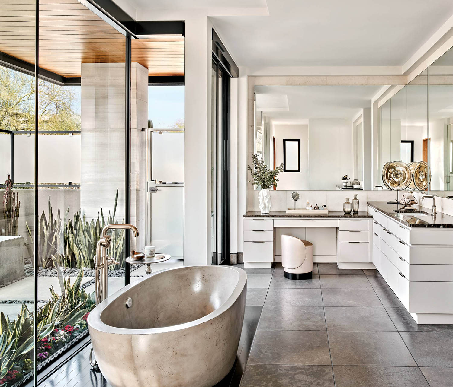 A concrete bathtub and side table sit on steel panels in a bathroom with mirrors and a white vanity.