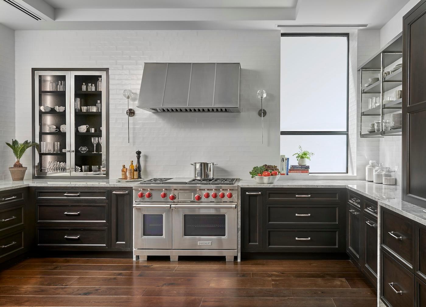 Sleek, modern kitchen with dark wood cabinets, marble countertops, and stainless steel appliances. A potted plant and kitchenware add a homely touch.