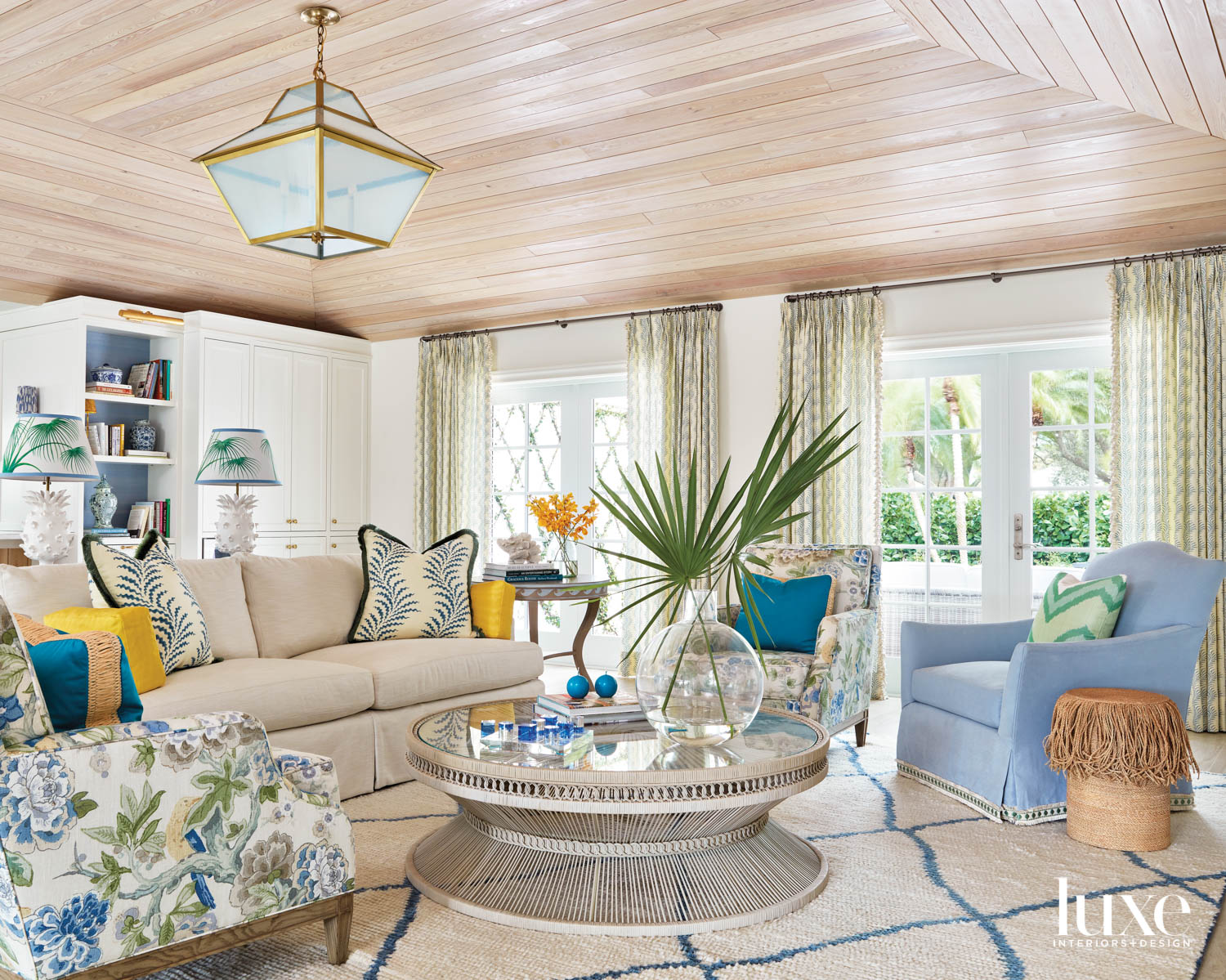 living area with ceiling lantern, cypress ceiling, white sofa, blue armchair, patterned armchair, striped rug and round rattan coffee table