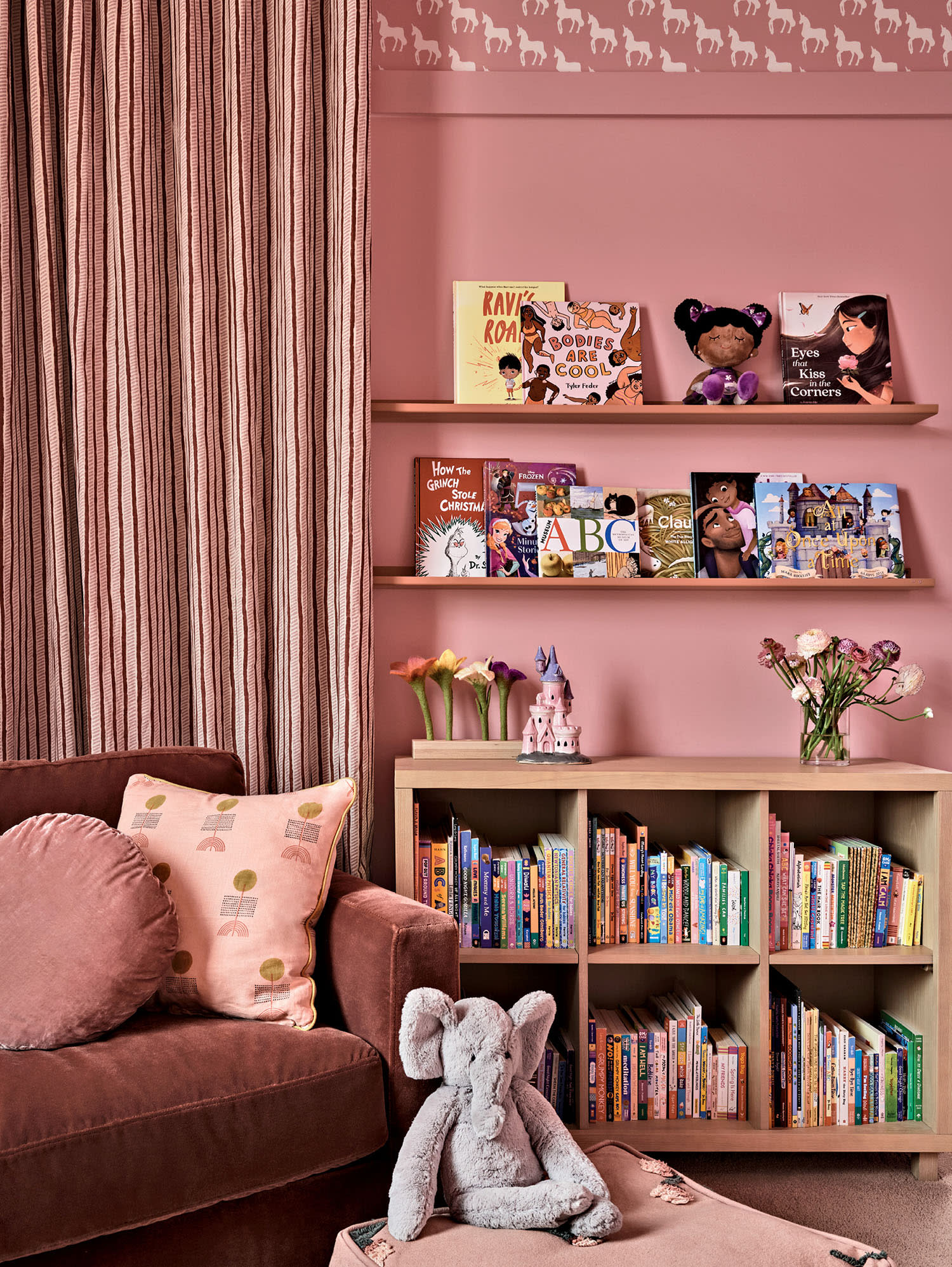 Cozy reading nook in a nursery with pink walls, striped curtains, and bookshelves. Plush elephant toy and colorful books create a warm, inviting atmosphere.