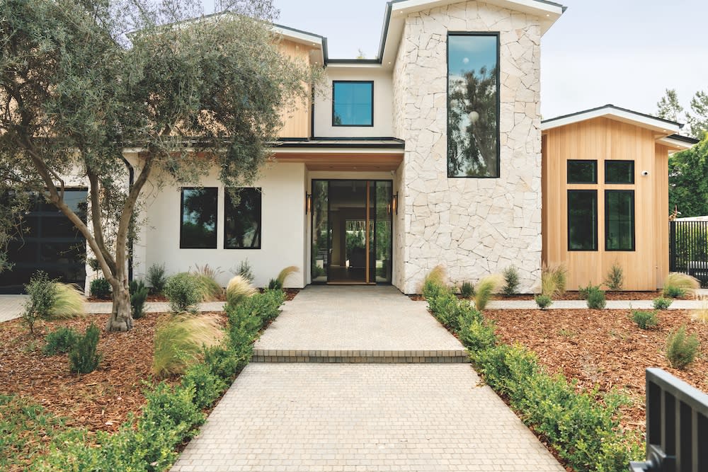 A contemporary home featuring a stone walkway surrounded by well-maintained landscaping, showcasing modern architectural design.